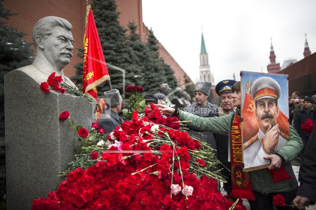 A woman holding a portrait of Stalin places flowers near the monument signifying Joseph Stalin's grave near the Kremlin wall marking the anniversary of Stalin's birth in Moscow's Red Square, Russia, Thursday, Dec. 21, 2017. (AP Photo/Alexander Zemlianichenko)
