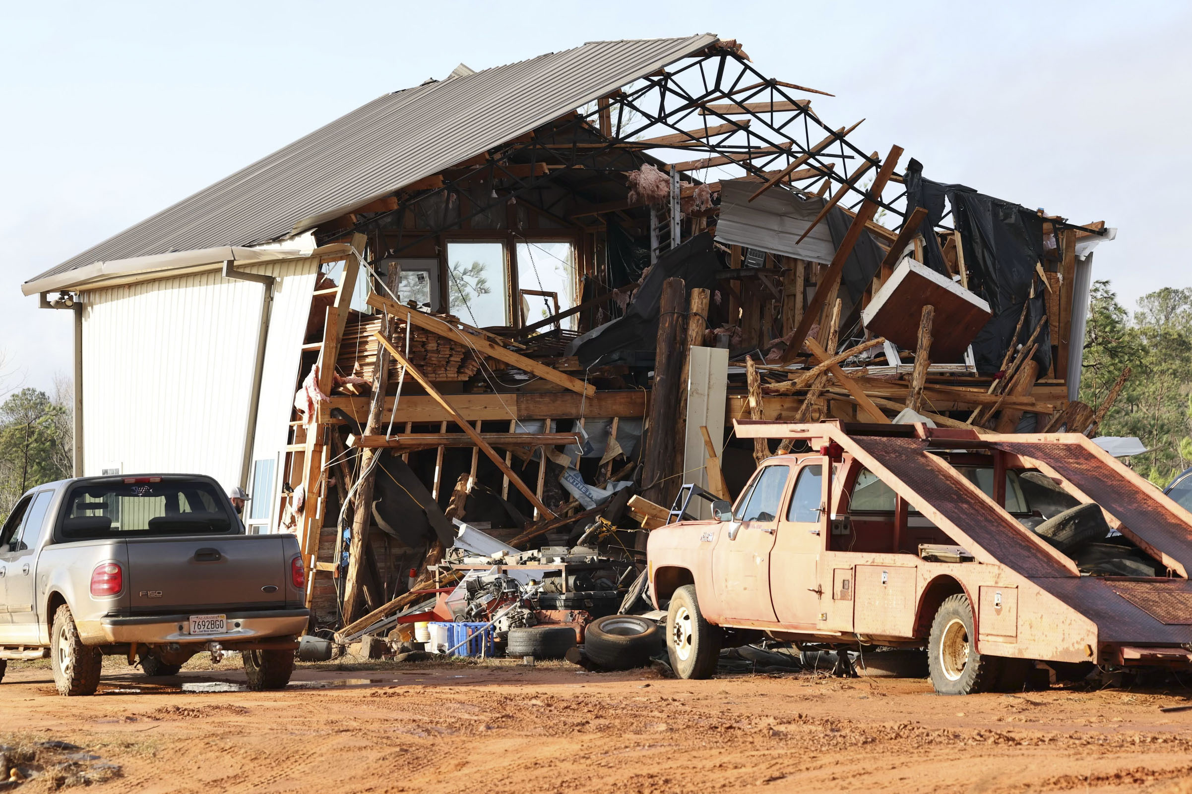 A home with a ripped-up roof and no front wall, with debris scattered on surrounding vehicles