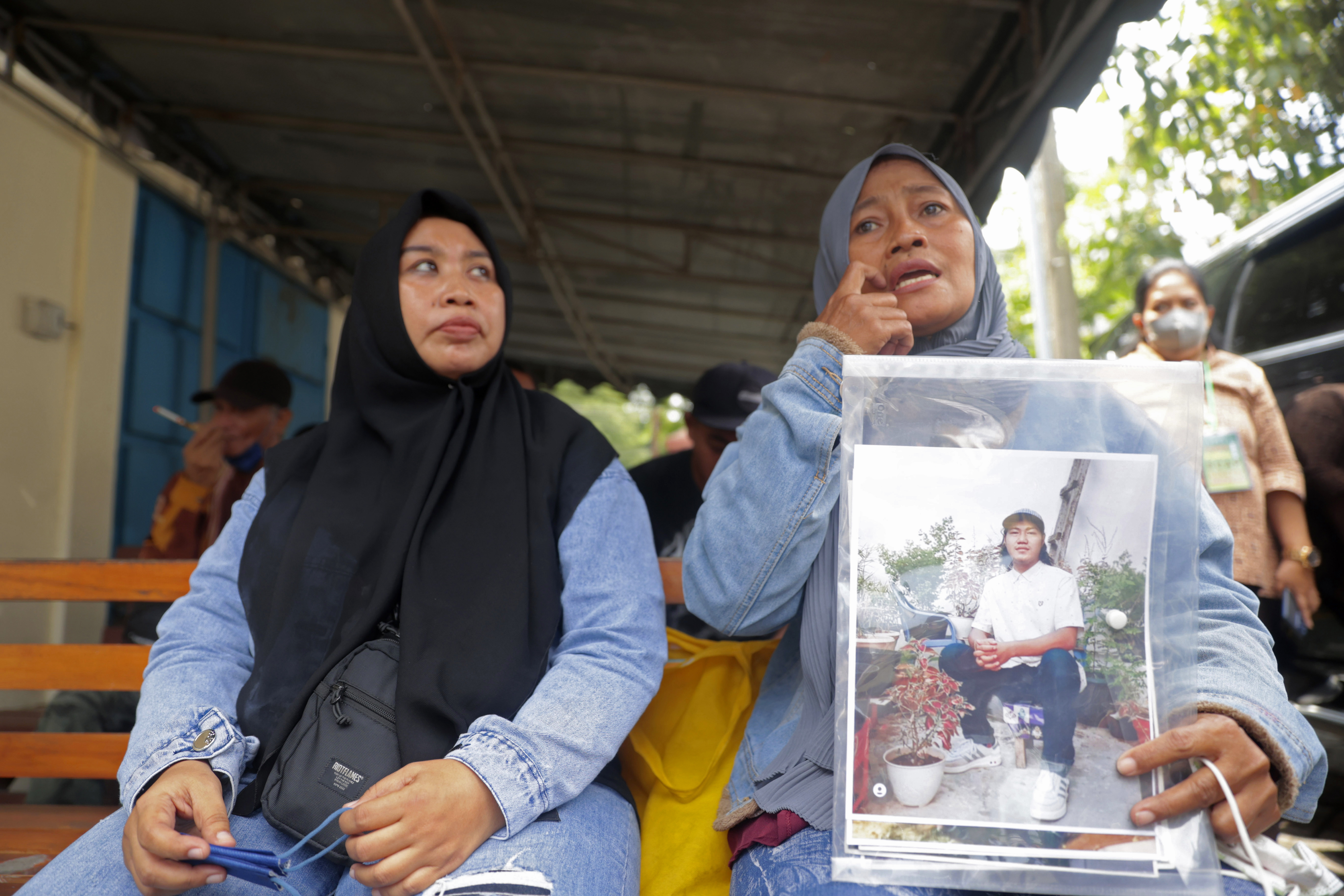 Rini Hanifah sitting on a wooden bench outside the Surabaya court holding a picture of her son Agus Riyansah who died in the October stampede. Rini is with a friend and she is crying.