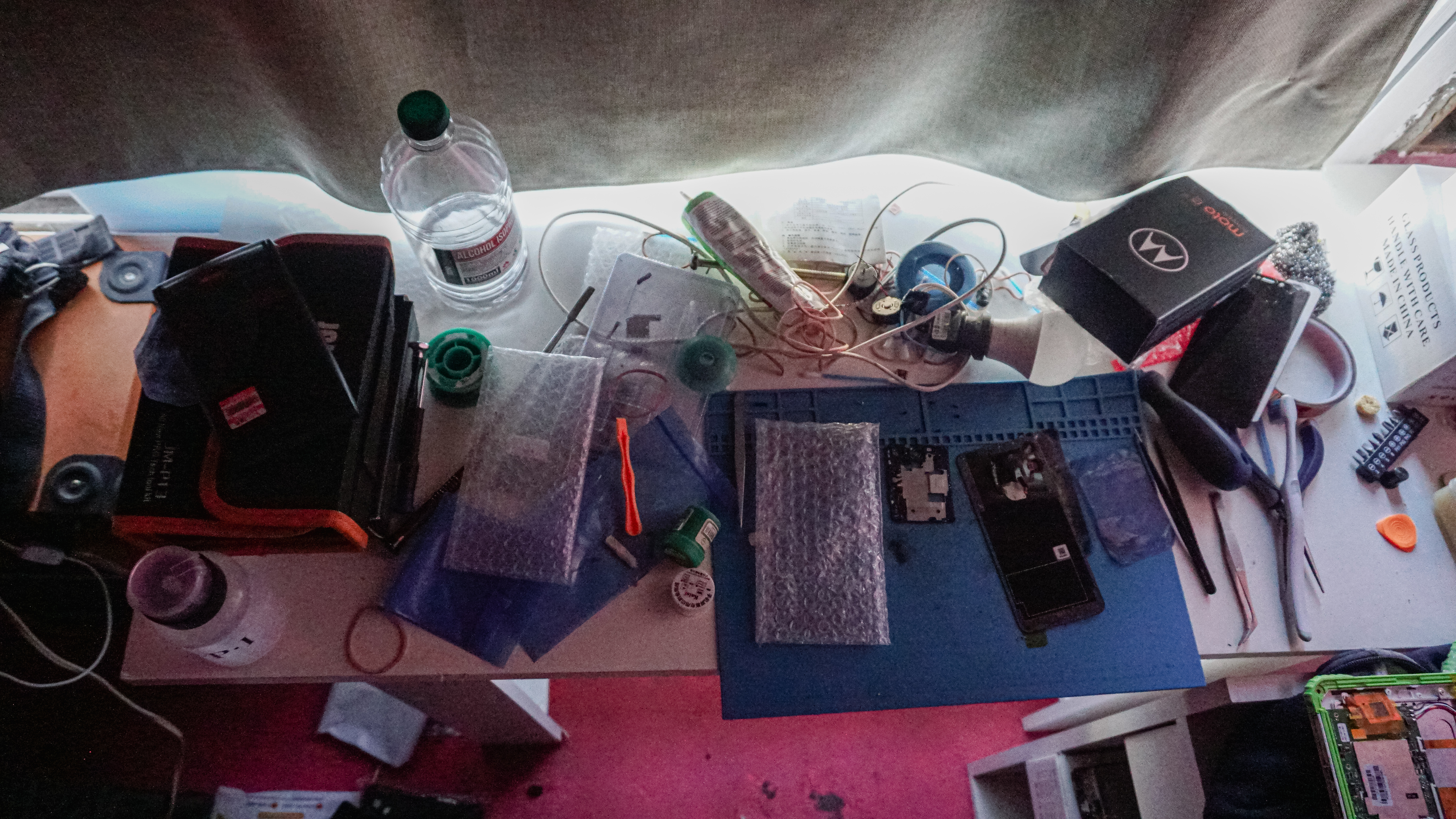 A photo of a table with a variety of things and tools includiung a phone that has been taken apart.