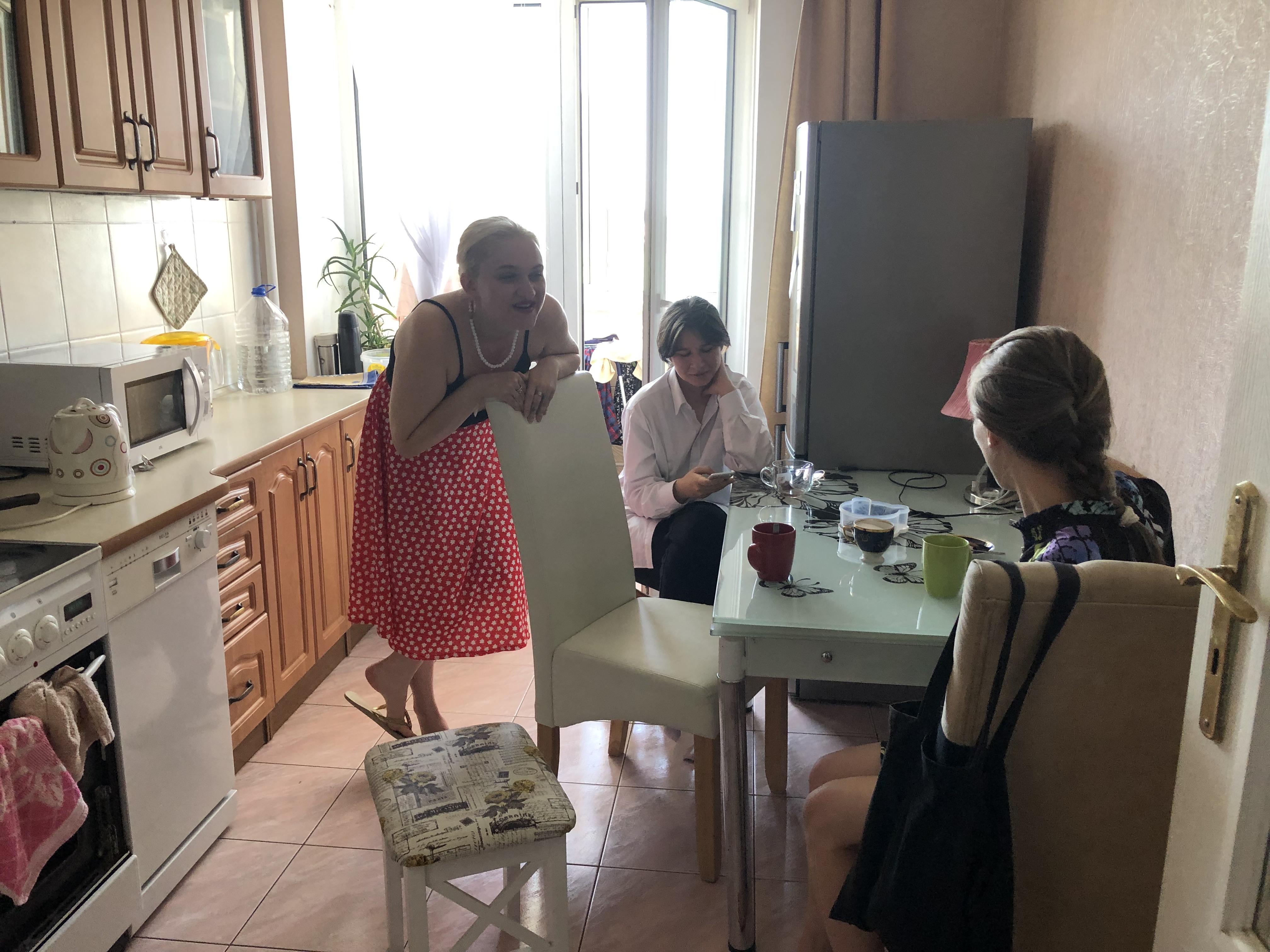 A photo of Mira having a conversation with two other people sitting at the kitchen table.