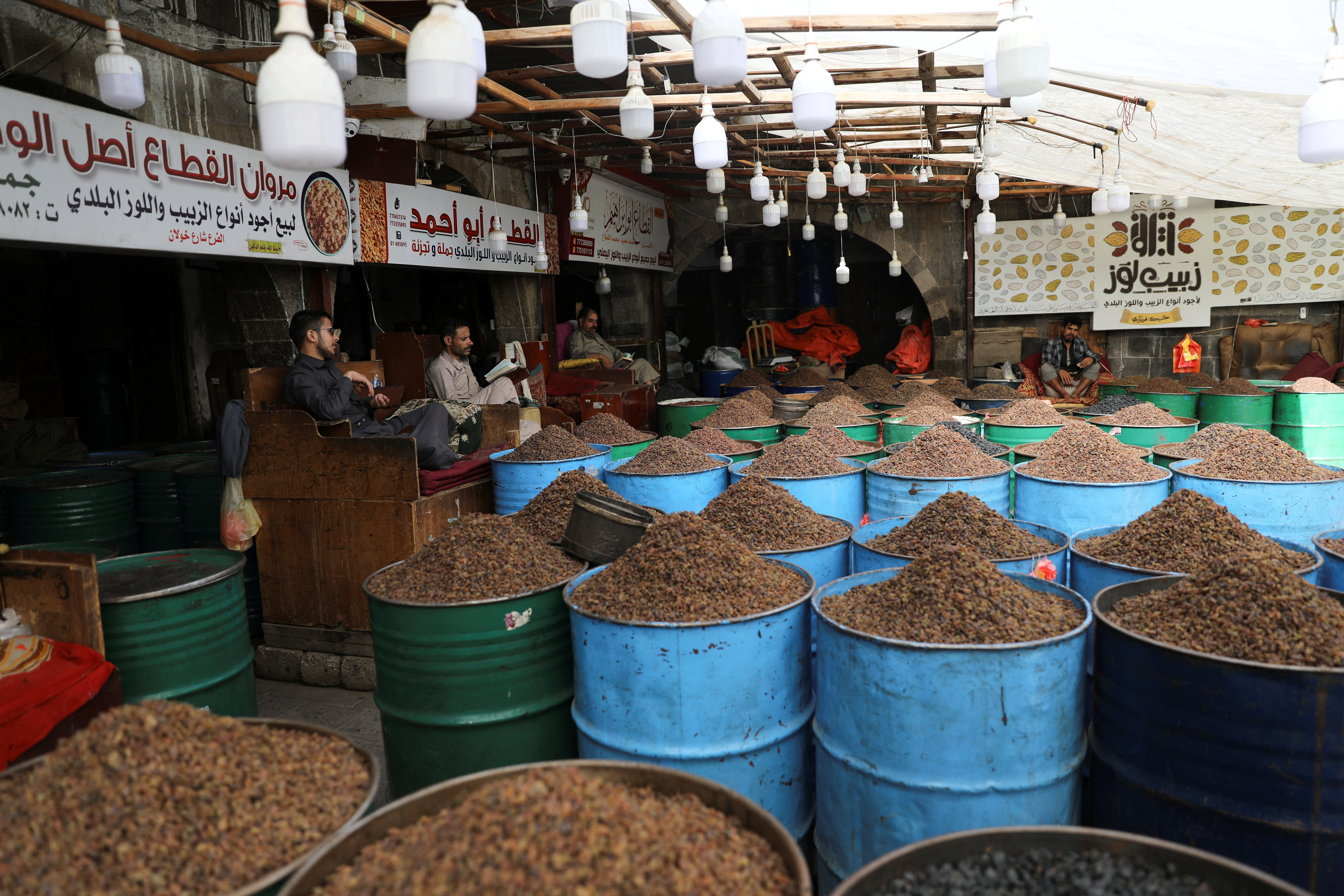 A photo of a market with barrels of raisins and people sitting in chairs behind the barrels.
