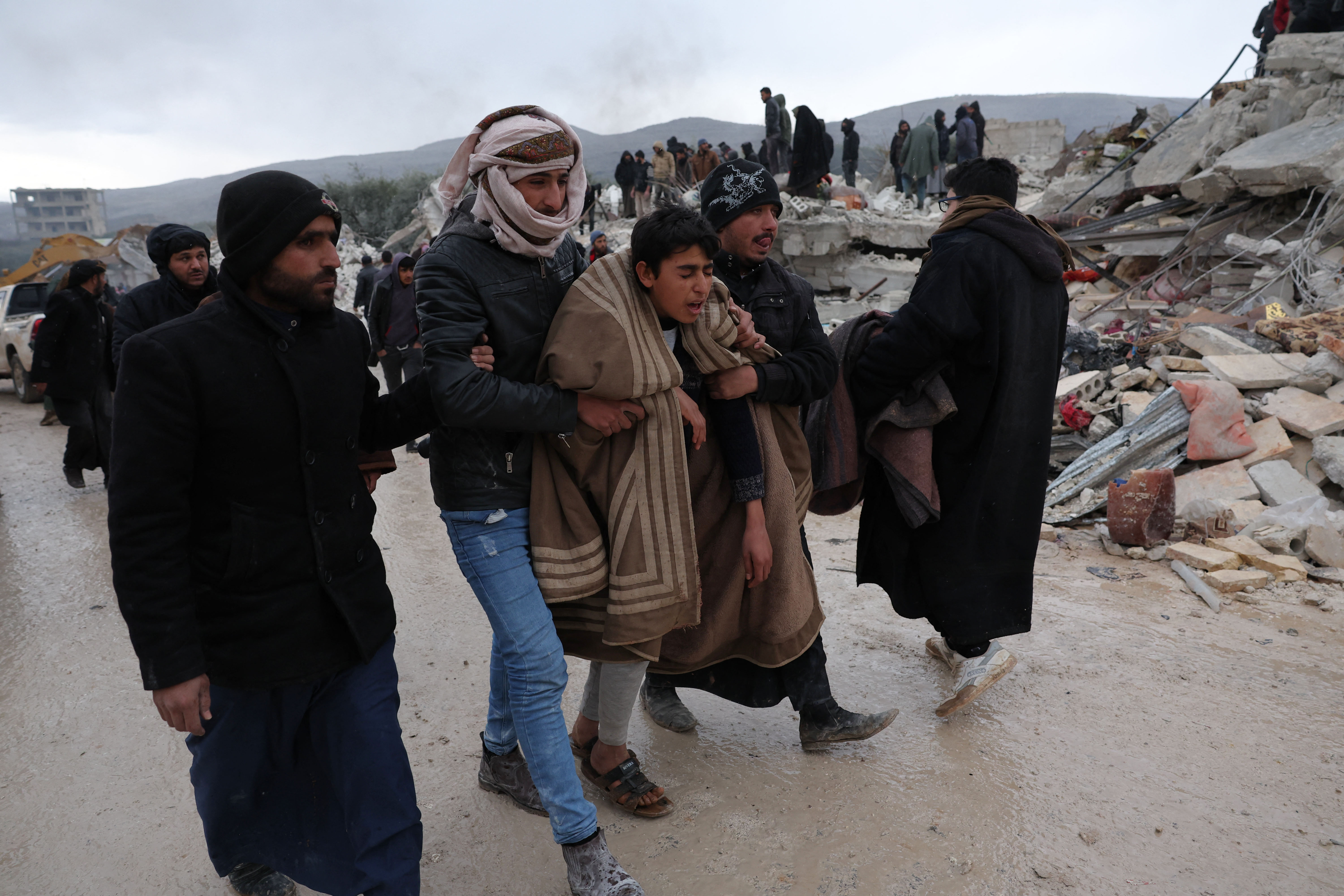 A youth is comforted as residents and rescuers search for victims and survivors following an earthquake in the village of Besnaya in Syria's rebel-held northwestern Idlib province on the border with Turkey, on February 6, 2022. - At least 1,293 people were killed and 3,411 injured across Syria today in an earthquake that had its epicentre in southwestern Turkey, the government and rescuers said. (Photo by OMAR HAJ KADOUR / AFP)