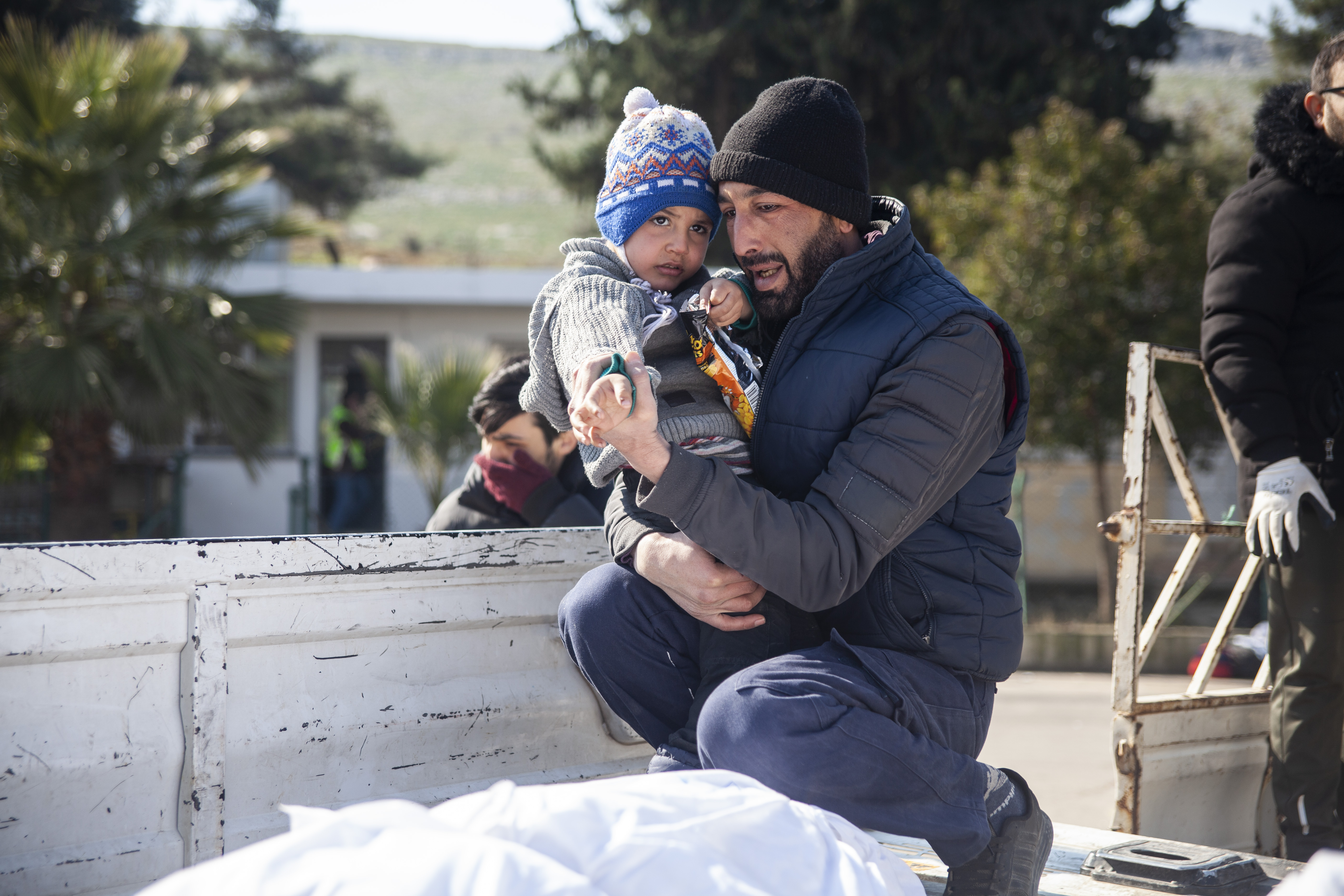 Father trying to explain to his young son that his mother is in the body bag on the truck