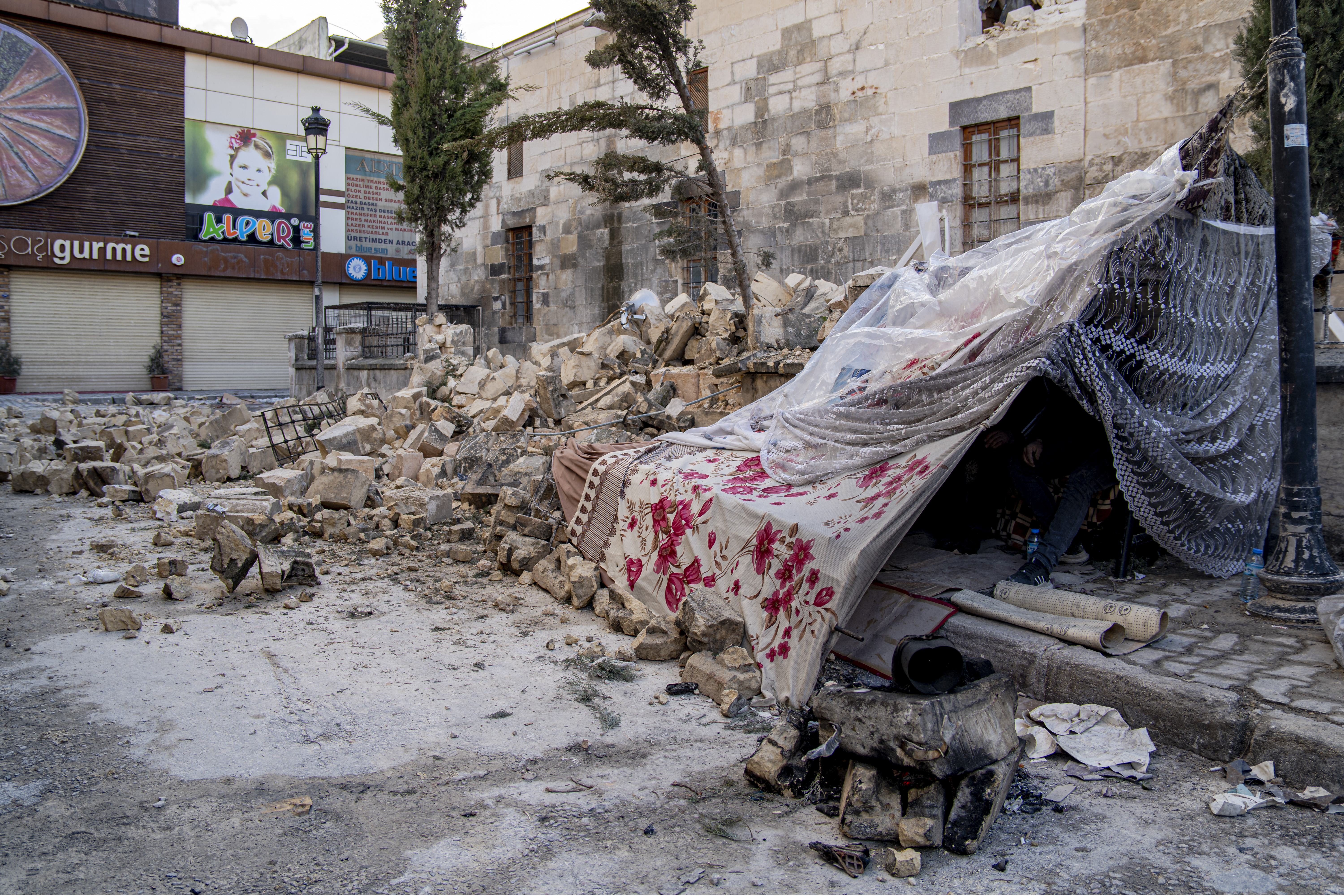 Two homeless men shelter in a makeshift tent next to a mosque