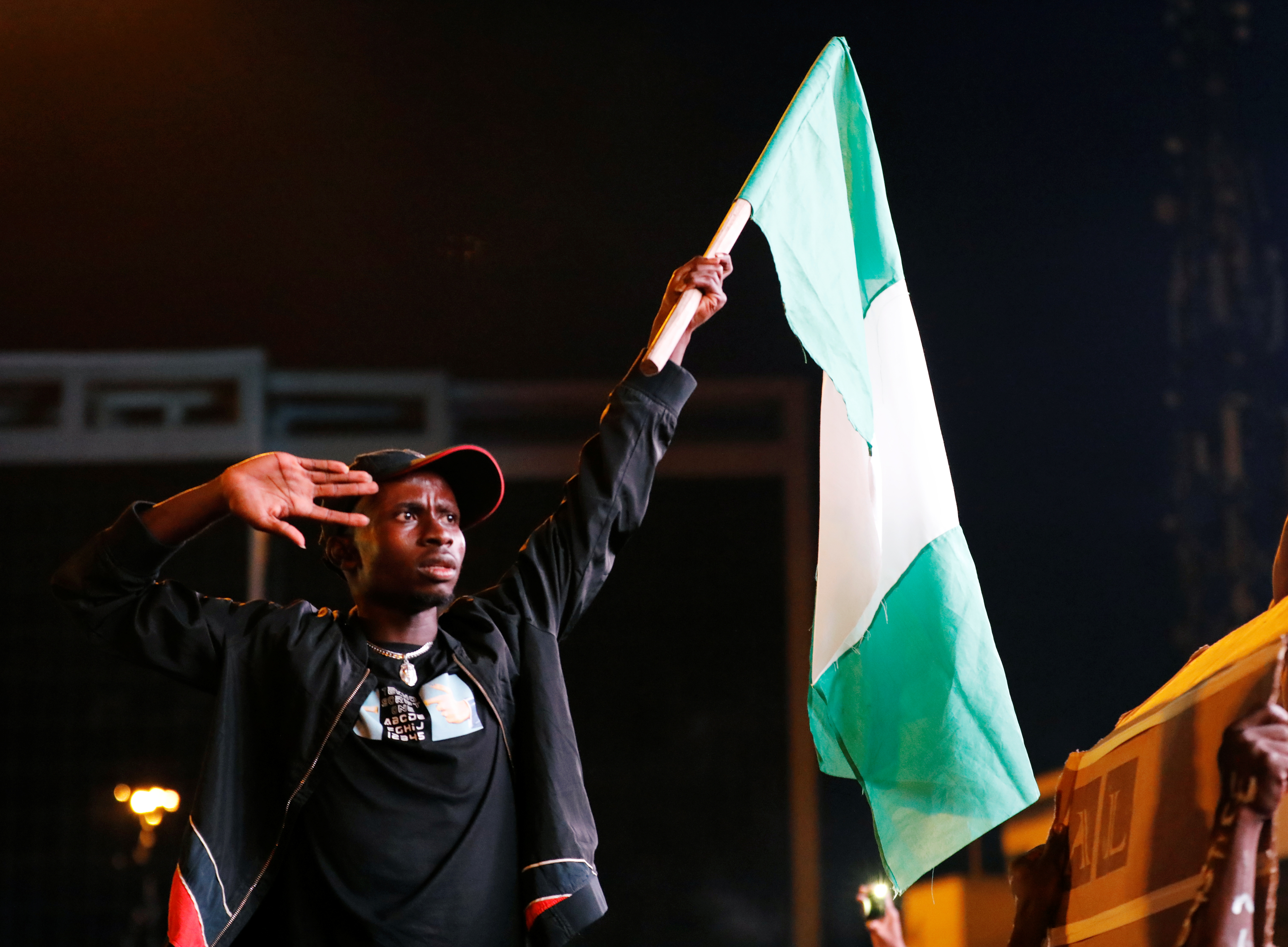 A demonstrator salutes as he raises the Nigerian flag during a protest over alleged police brutality
