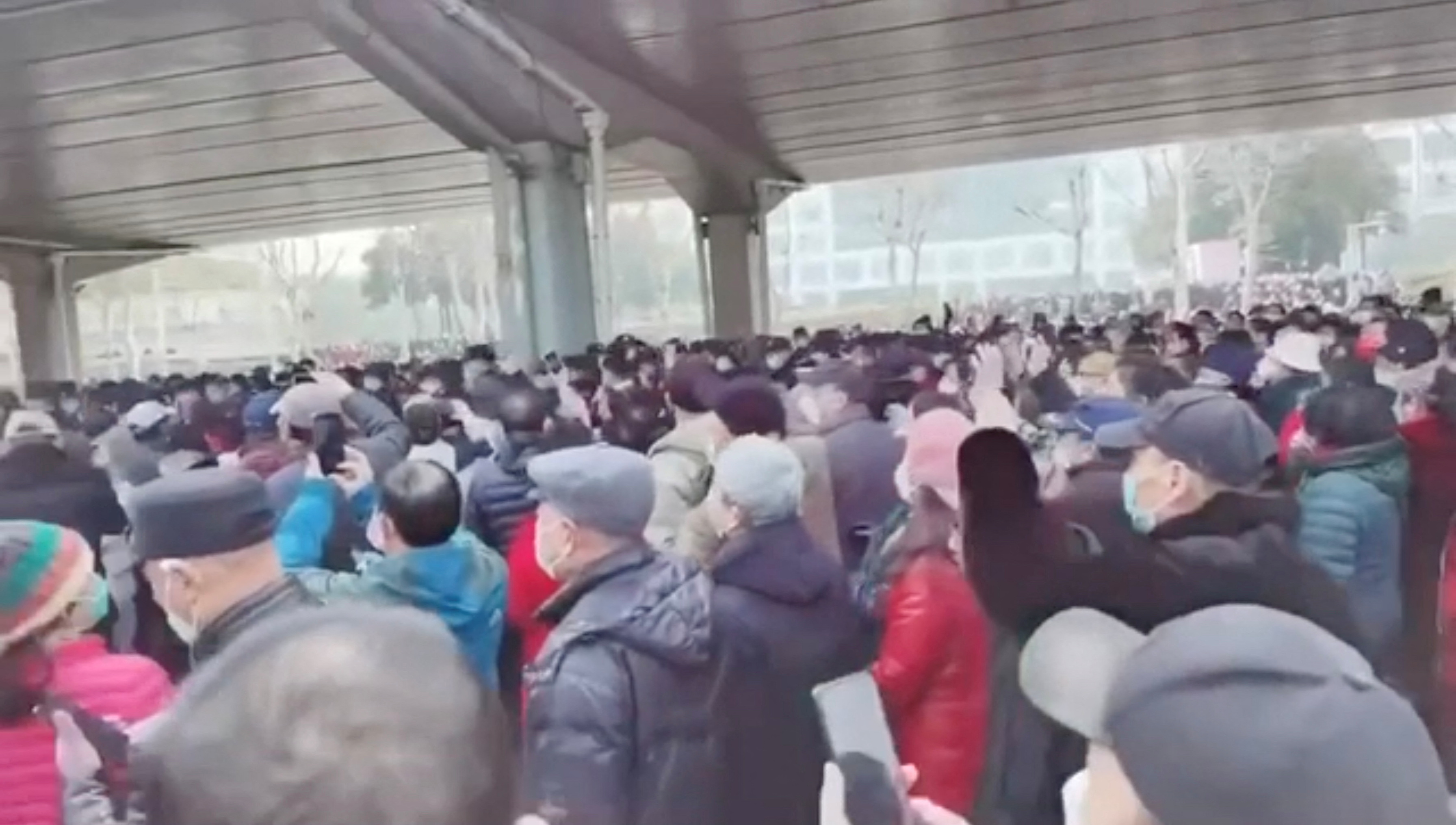 A crowd of people in winter clothing gathering beneath an underpass in Wuhan. Some have grey hair