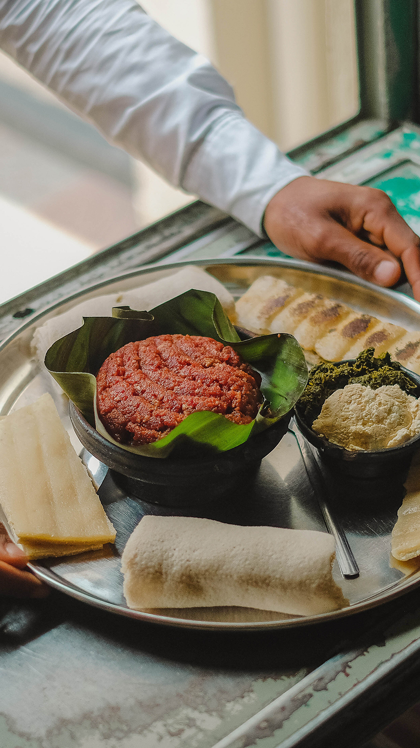 A waiter's hads at the pass taking a prepared kitfo tray from the pass out to a cusomer