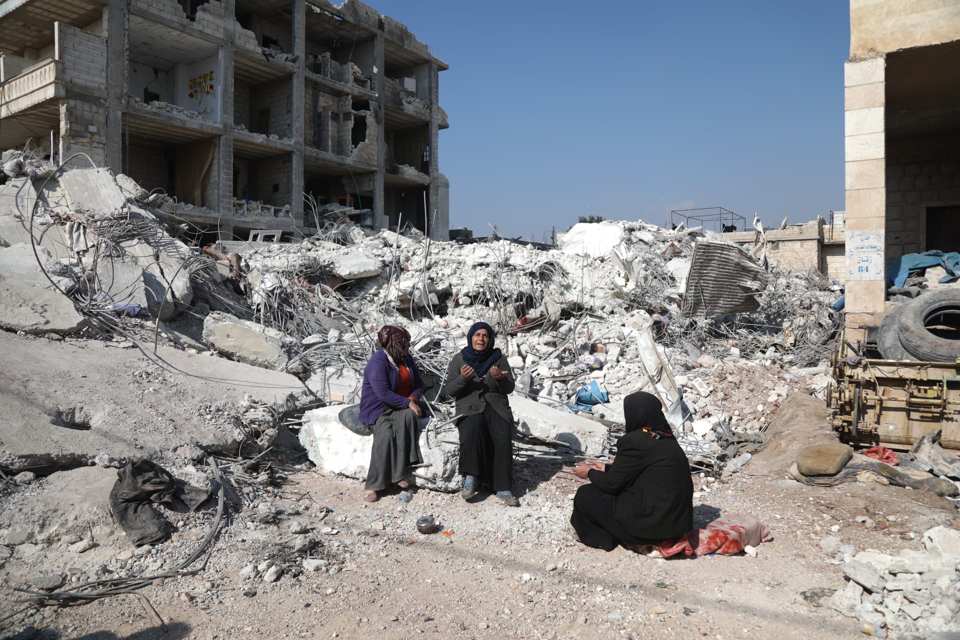 Asmaa' Kousa holds her hands up in prayer as she sits atop the rubble of her home.