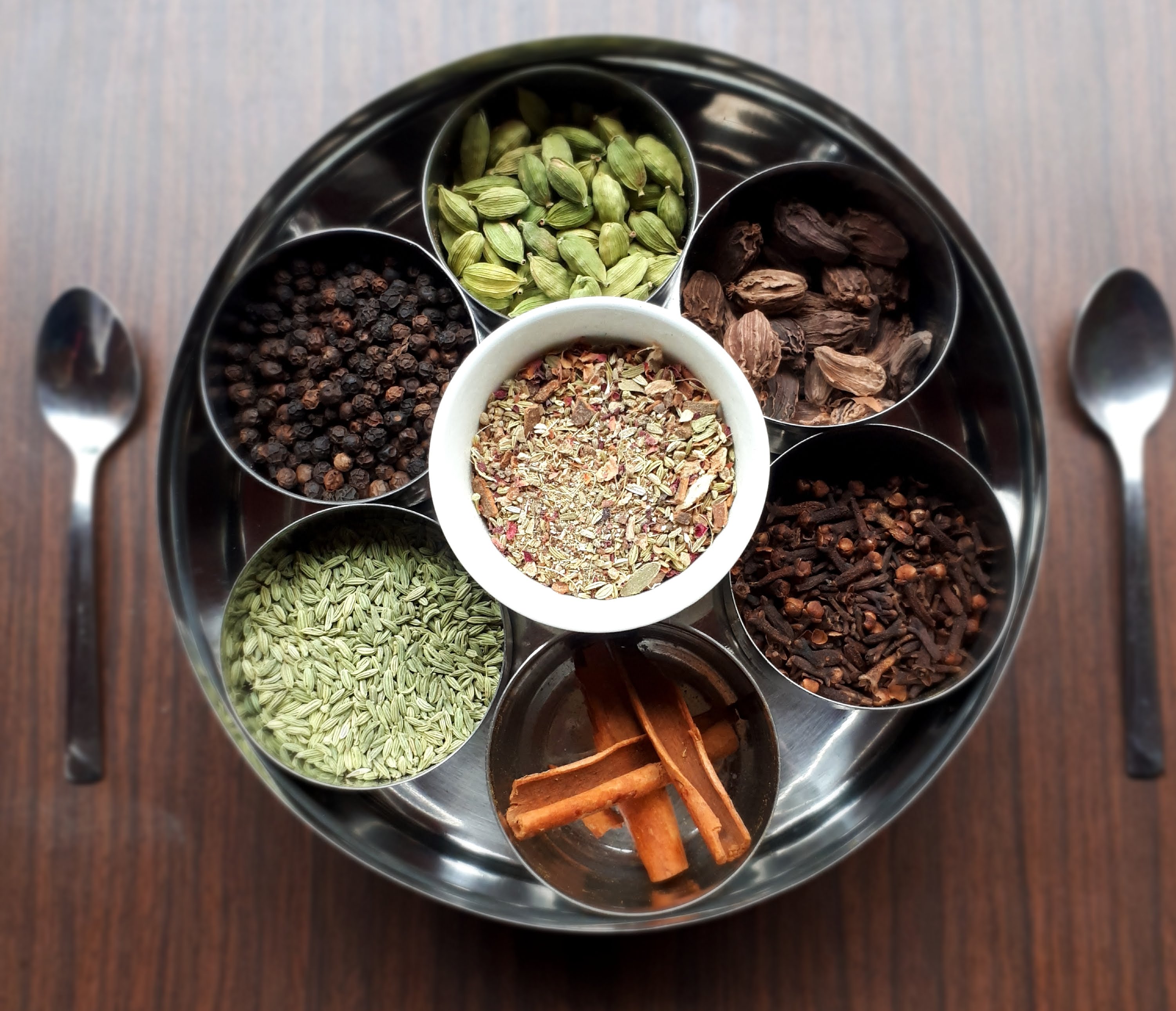 A shot of a masala daba, with seven smaller pots of spices in a larger metal container
