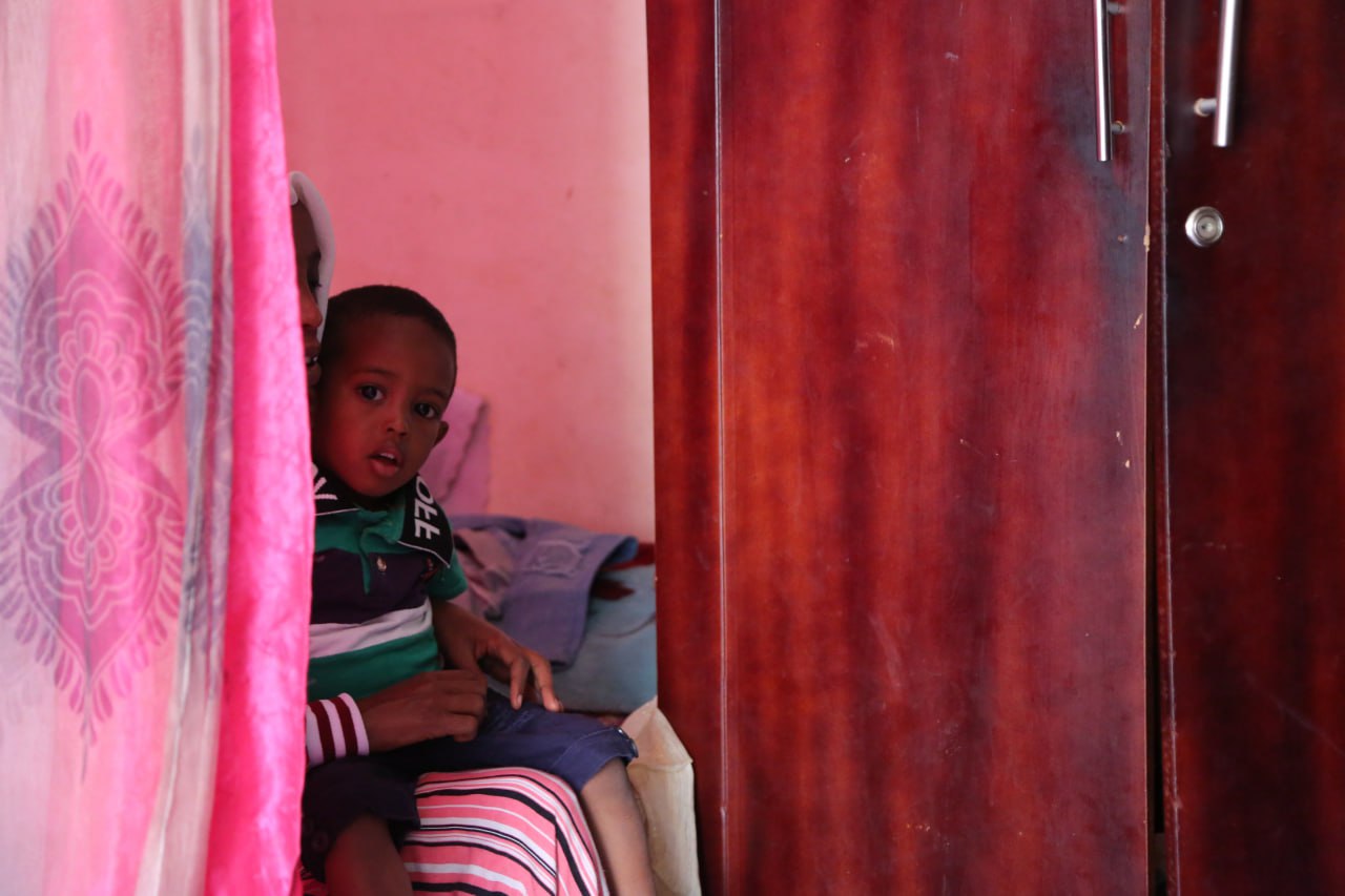 A photo of a woman behind a curtain holding her son on her lap.