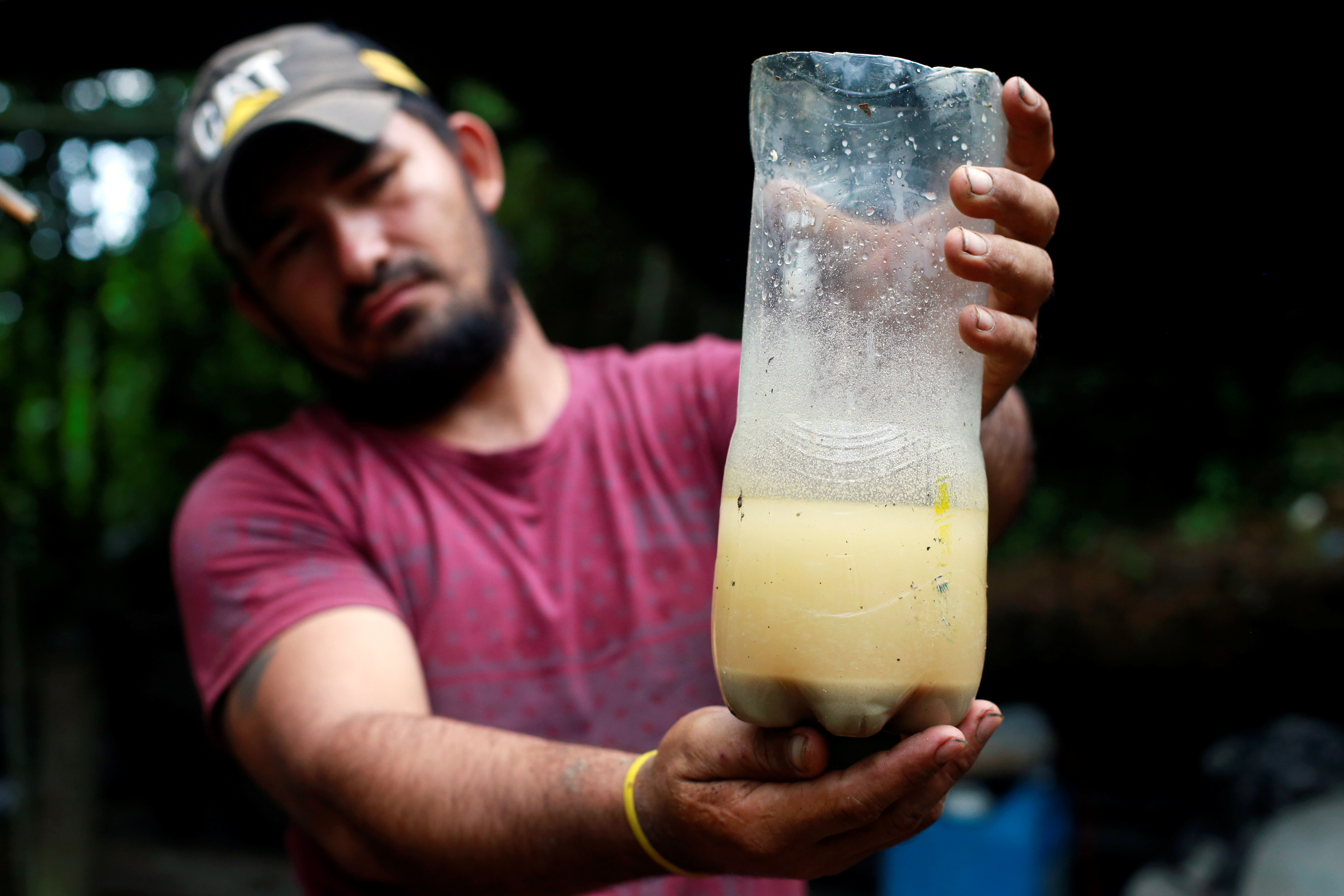 A man holds out a plastic bottle with a yellow-ish liquid inside, with sediment forming at the bottom