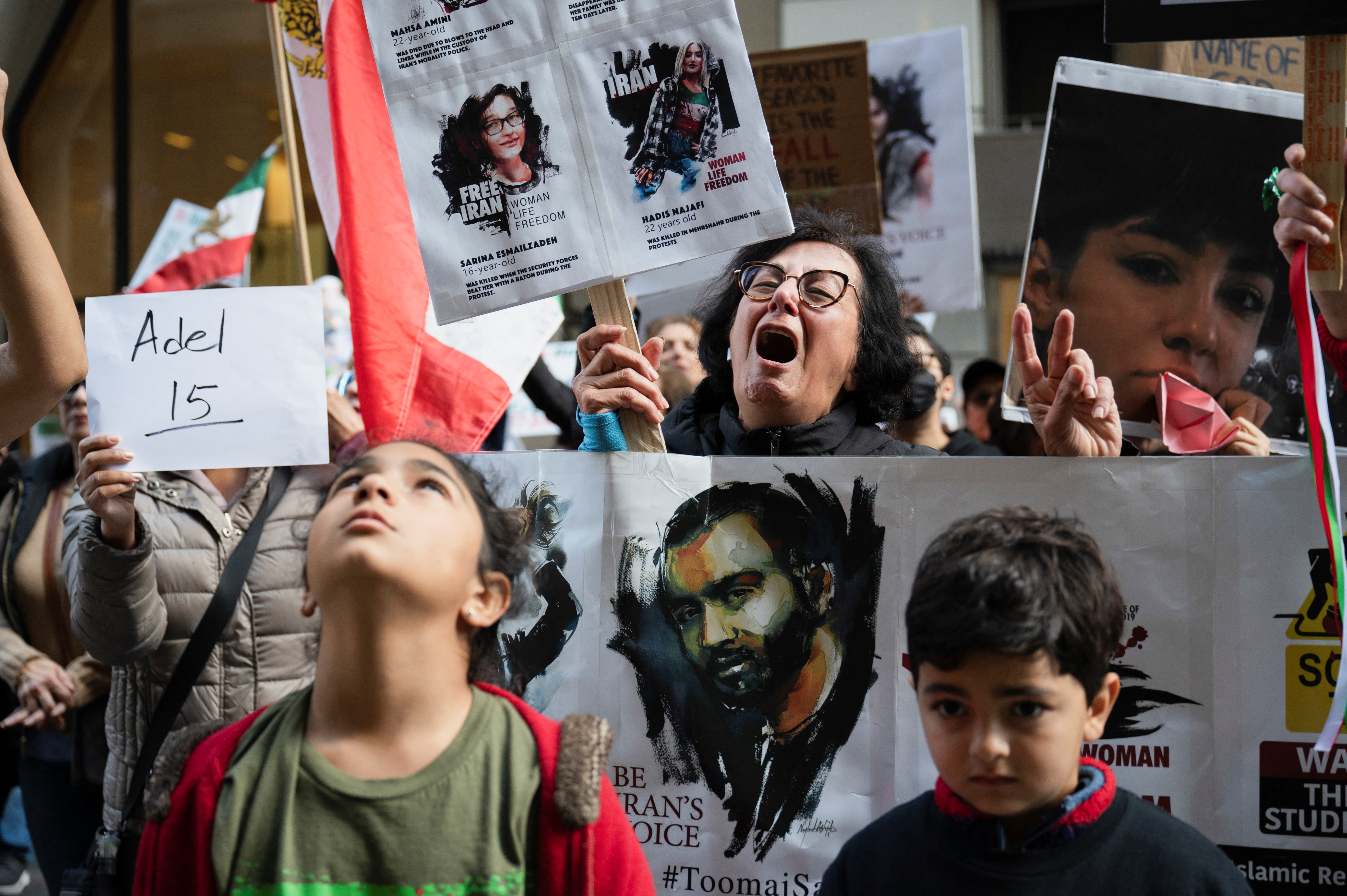 A child in the foreground looks up as an adult behind her carries a sign and shouts