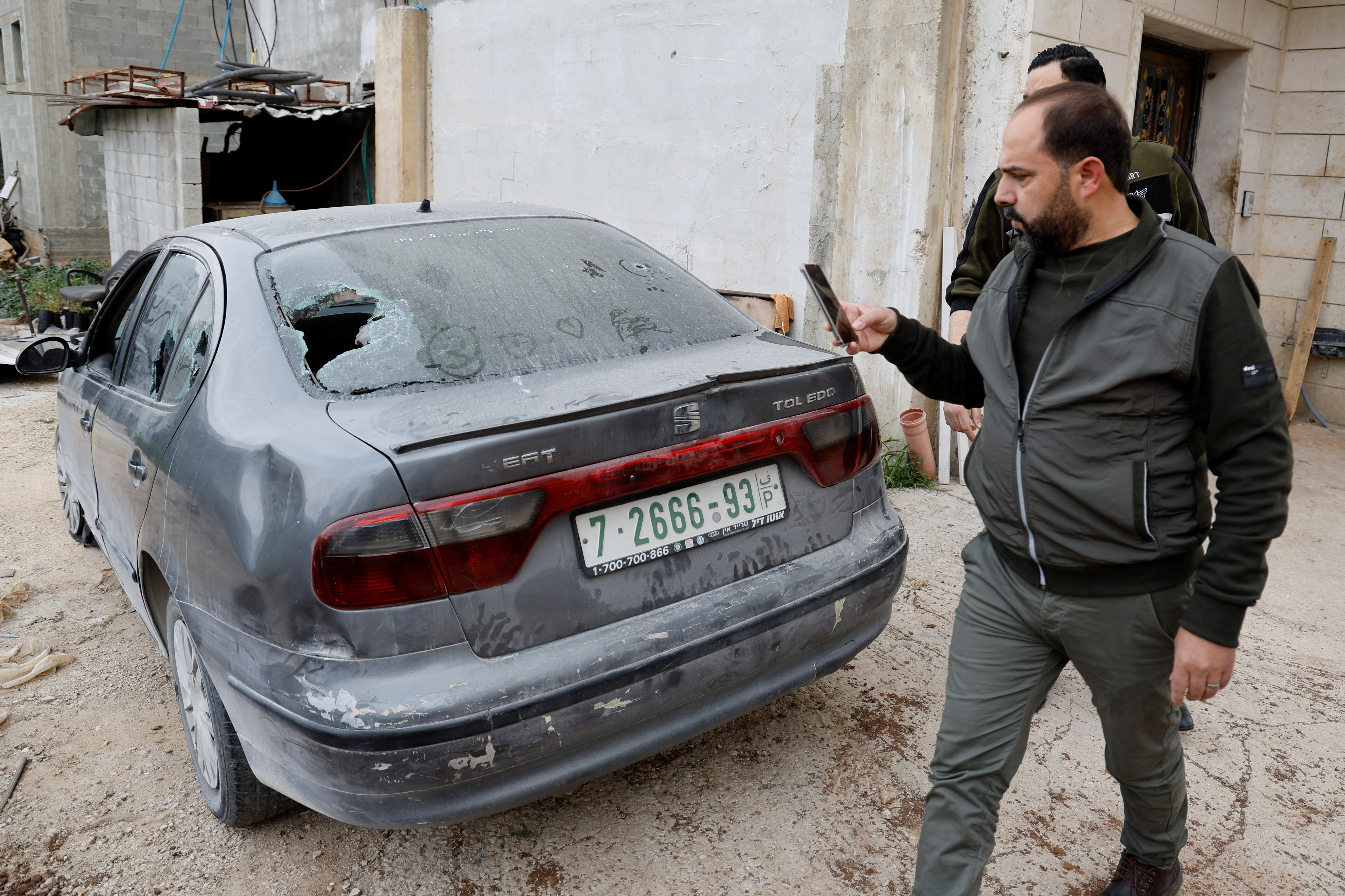 A man takes pictures of a car with a bullet hole in its back windshield