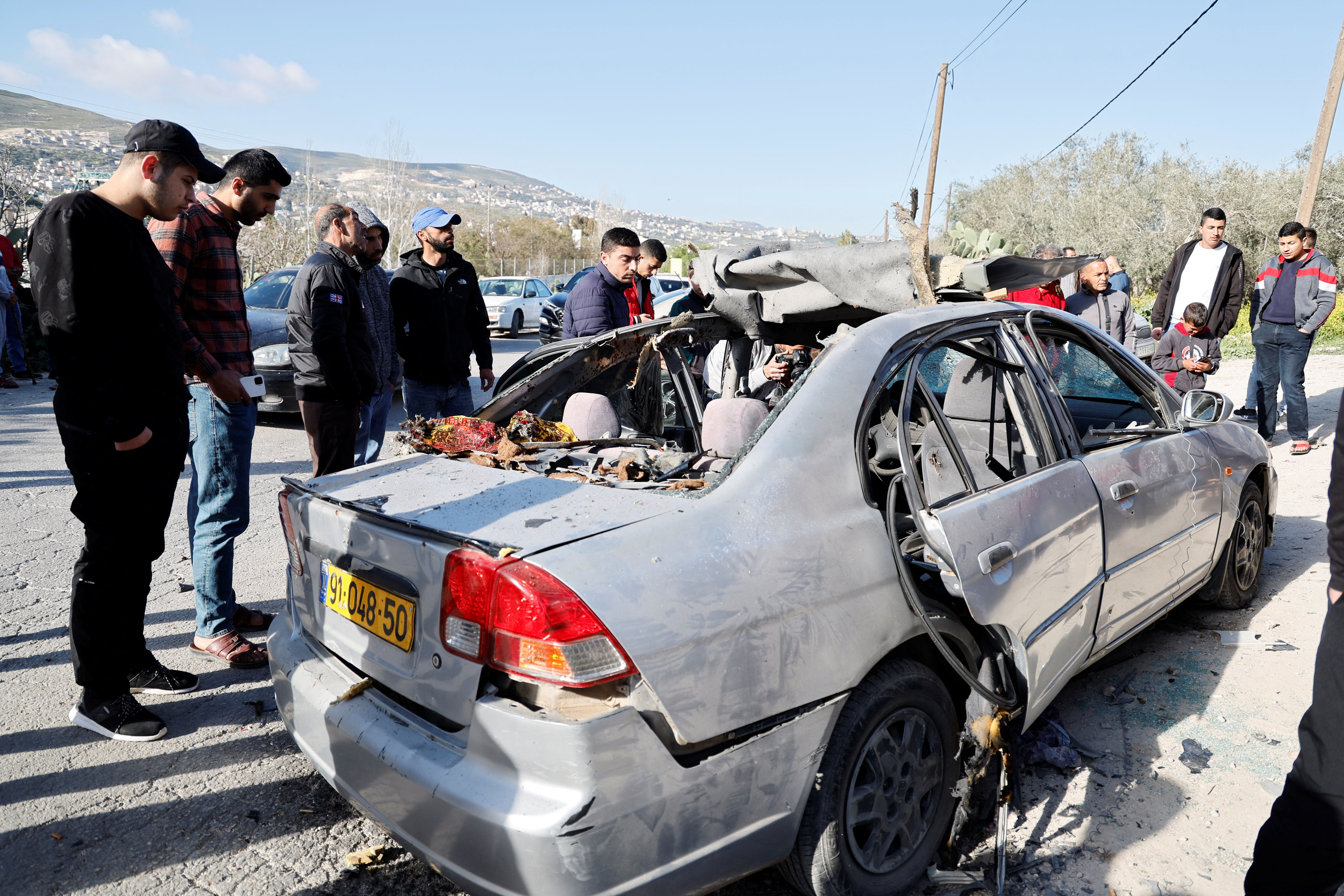 A group of people look at a car damaged in a shoot-out