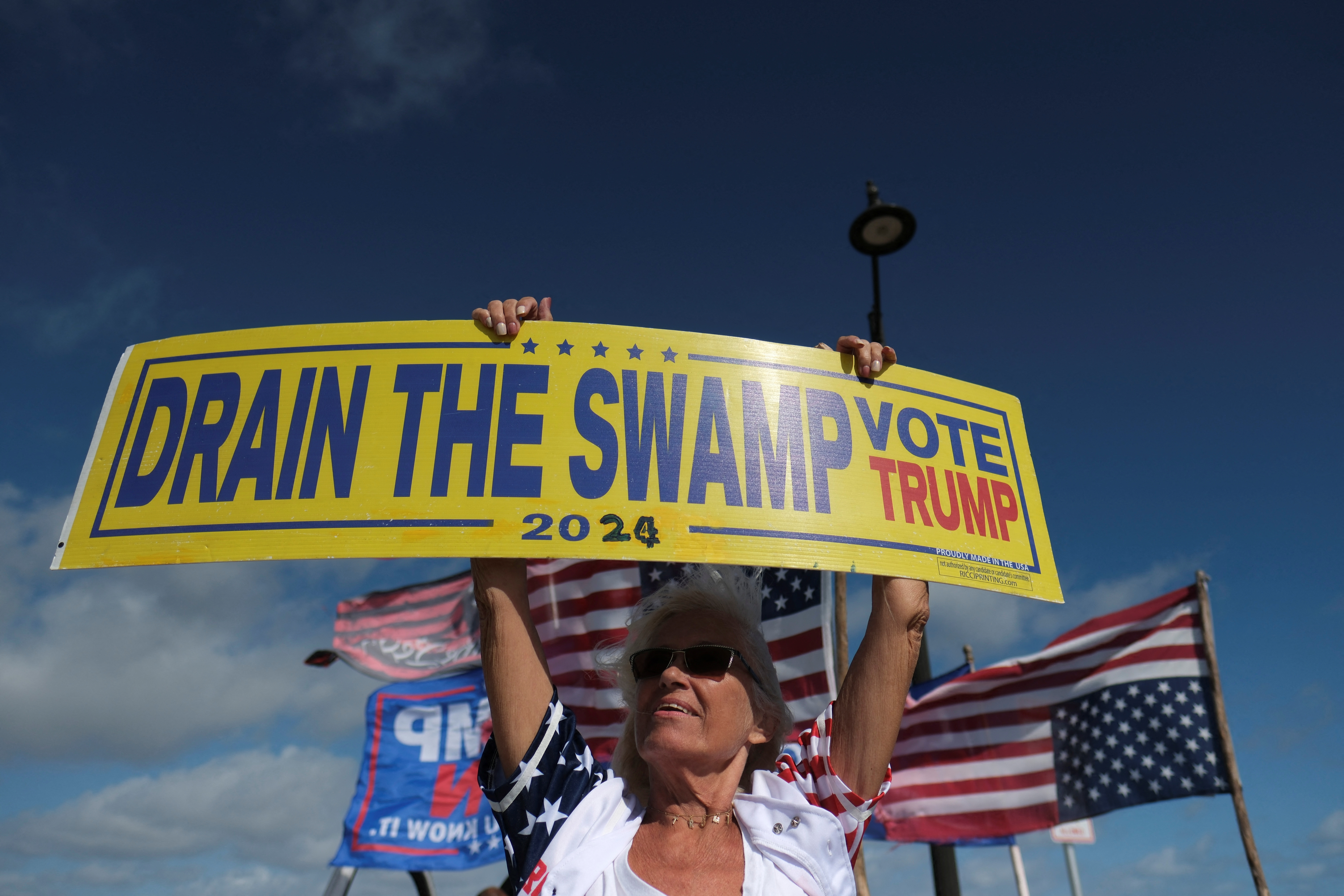 Trump supporter holding a sign that says "Drain the swamps, Vote Trump."