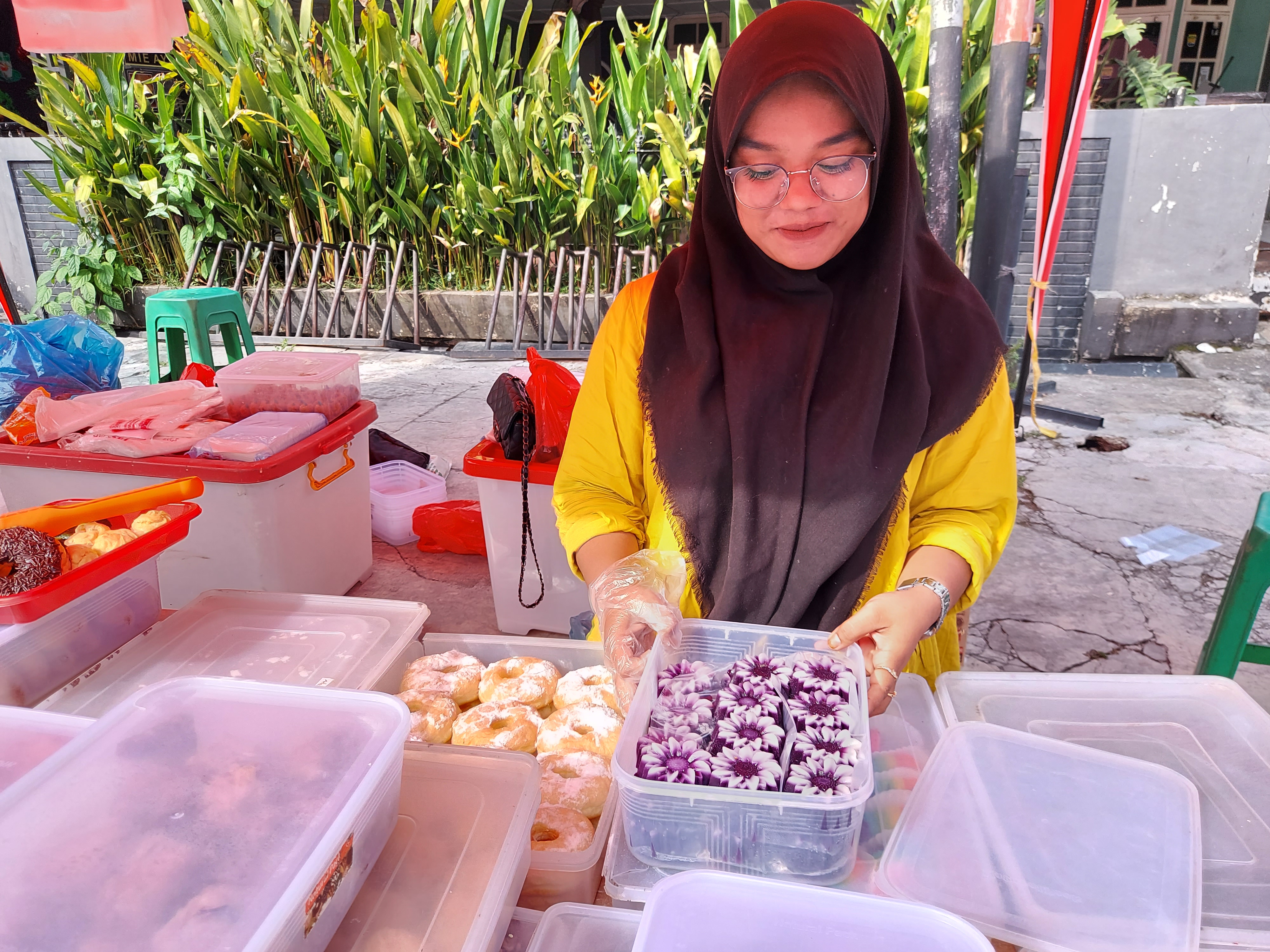Naila holds a plastic container filled with fuchsia-coloured takjil. She is smiling.