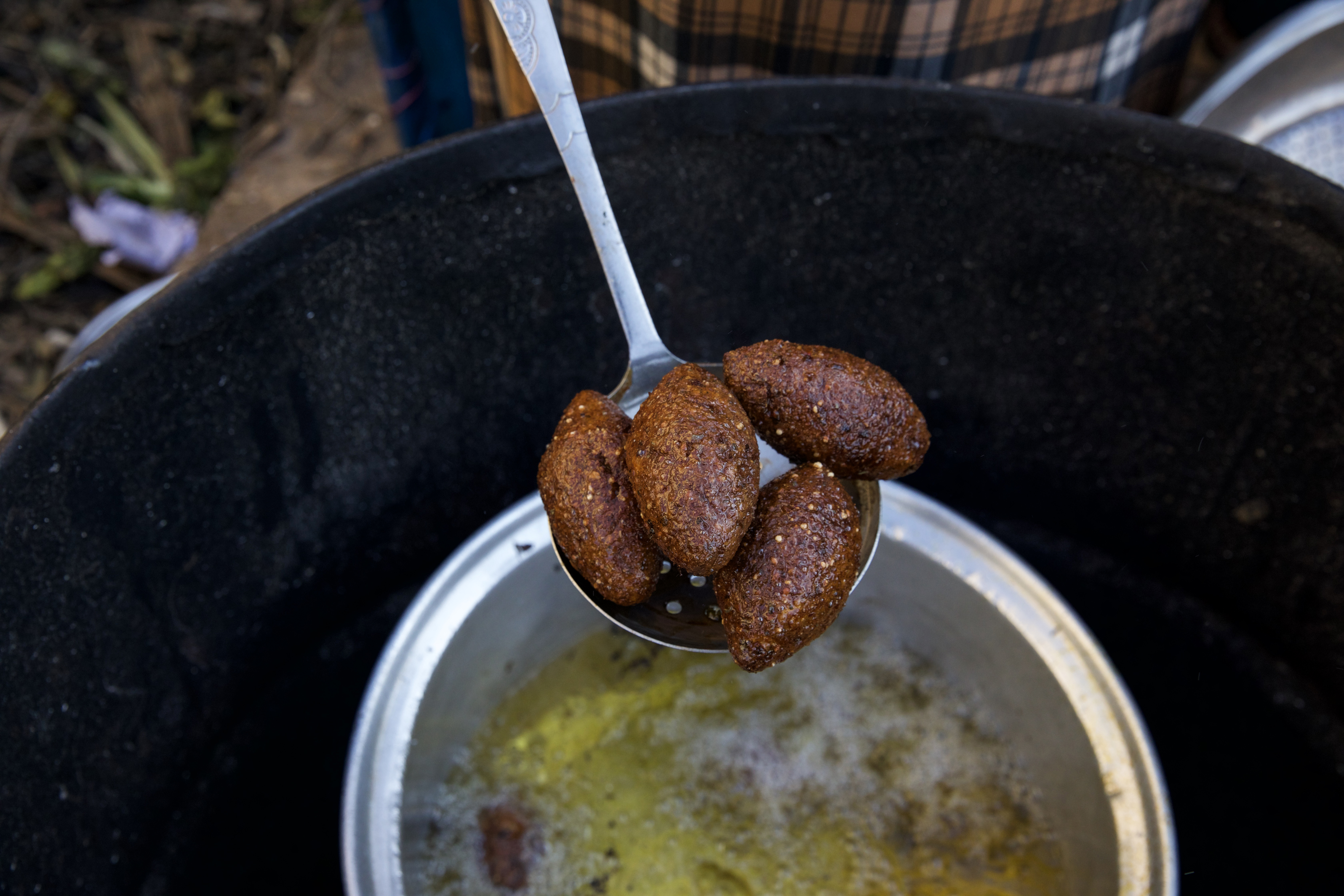 A slotted spook lifts out a scoop of kibbes from the hot oil
