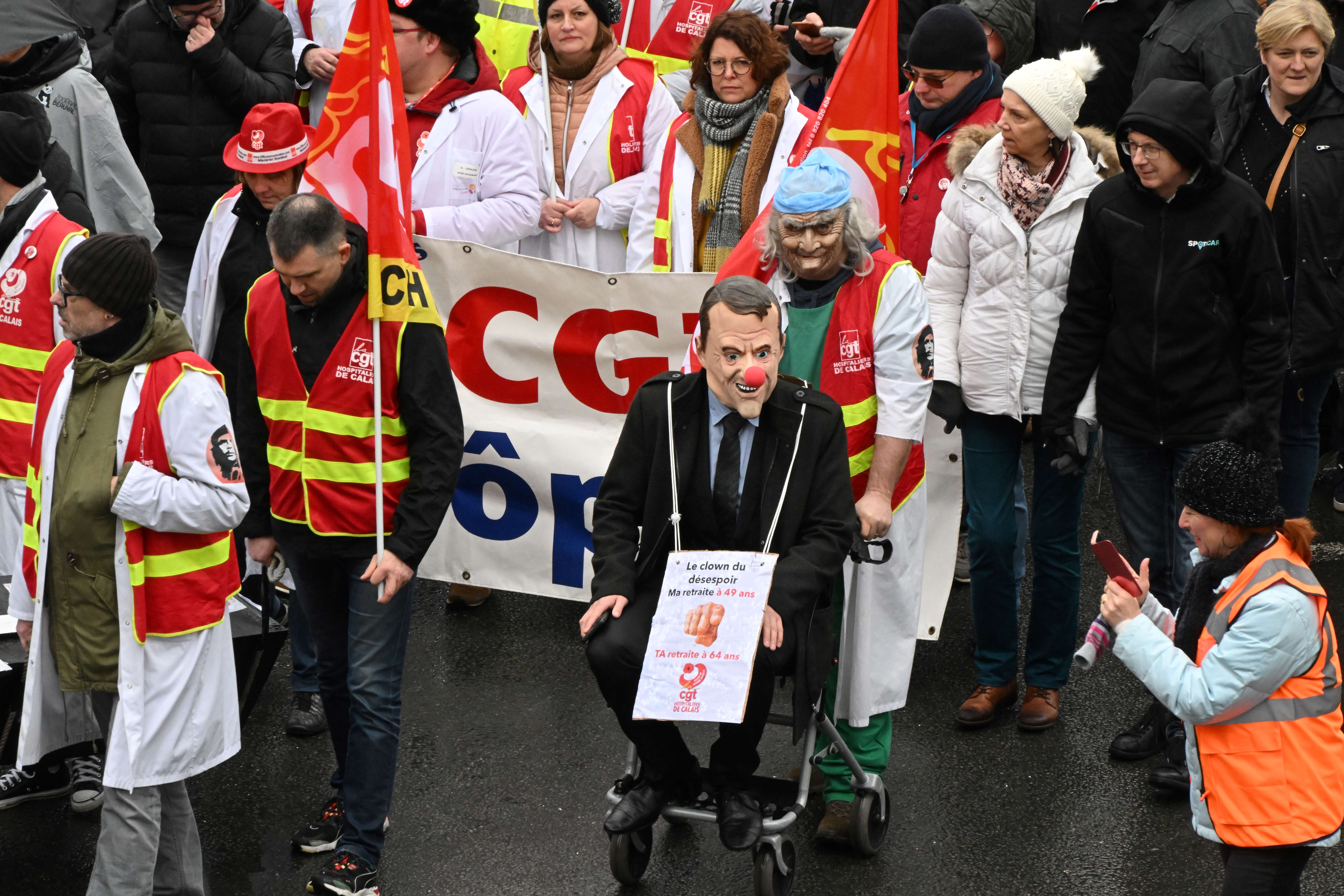 A man wearing a mask depicting French president Emmanuel Macron is seen on a wheelchair during a rally in Dunkirk, northern France, on March 7, 2023, as part of a nationwide action day against French President's pension reform and its postponement of the legal retirement age from 62 to 64. - Unions have vowed to bring the country to a standstill over the proposed changes, which include raising the retirement age from 62 to 64 and increasing the number of years workers have to make contributions for a full pension.