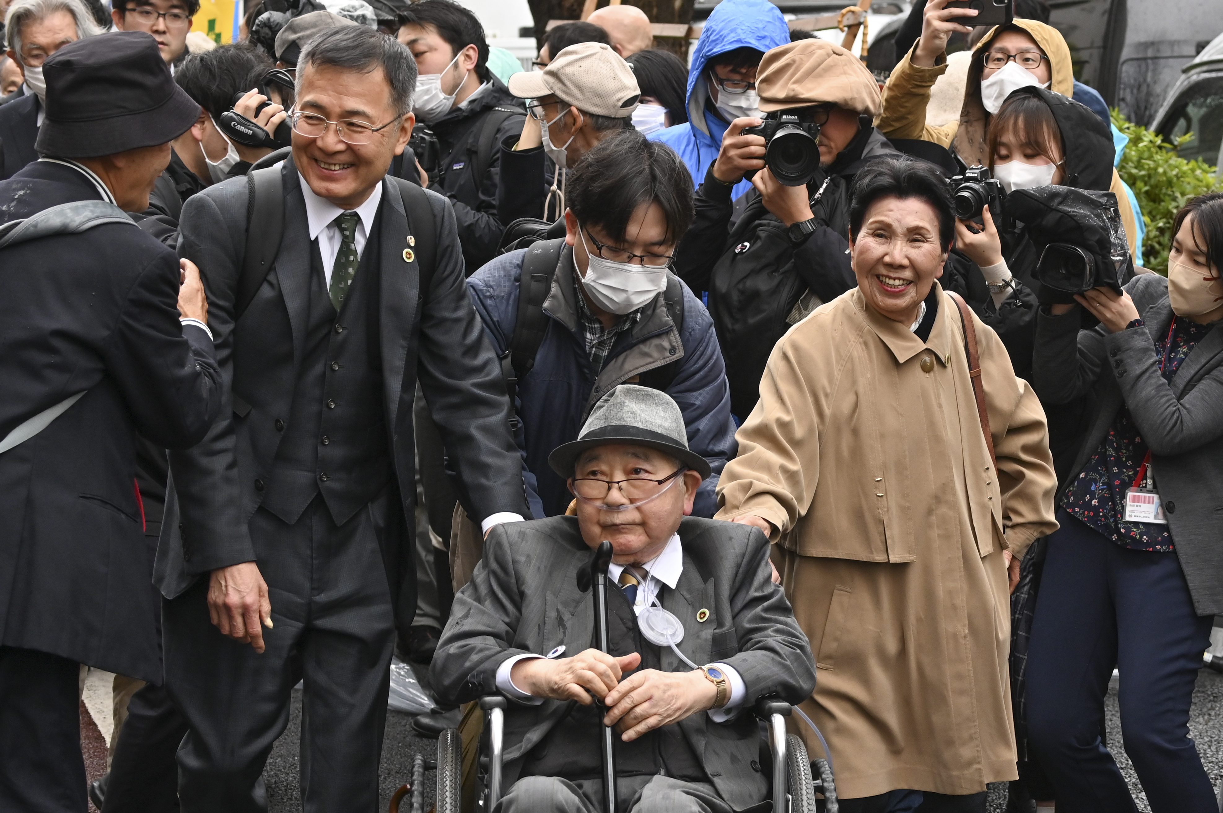Iwao Hakamada attends court in Tokyo with his family and supporters. He is a wheelchair. and wearing glasses His sister is next to him and smiling as she walks.