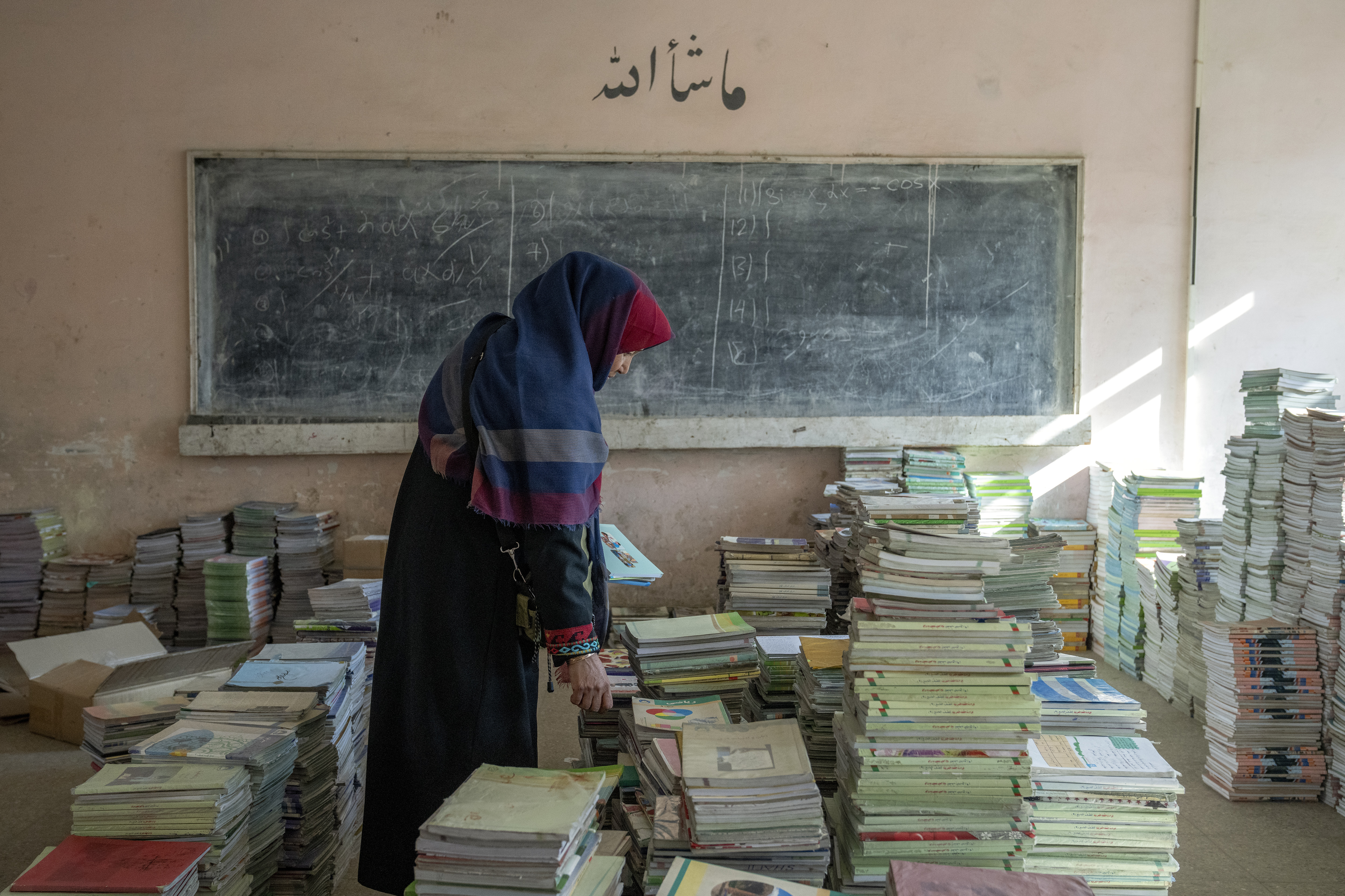 Amanah Nashenas, a 45-year-old Afghan teacher, collects books in a school in Kabul, Afghanistan, on December 22, 2022 [Ebrahim Noroozi/AP Photo]