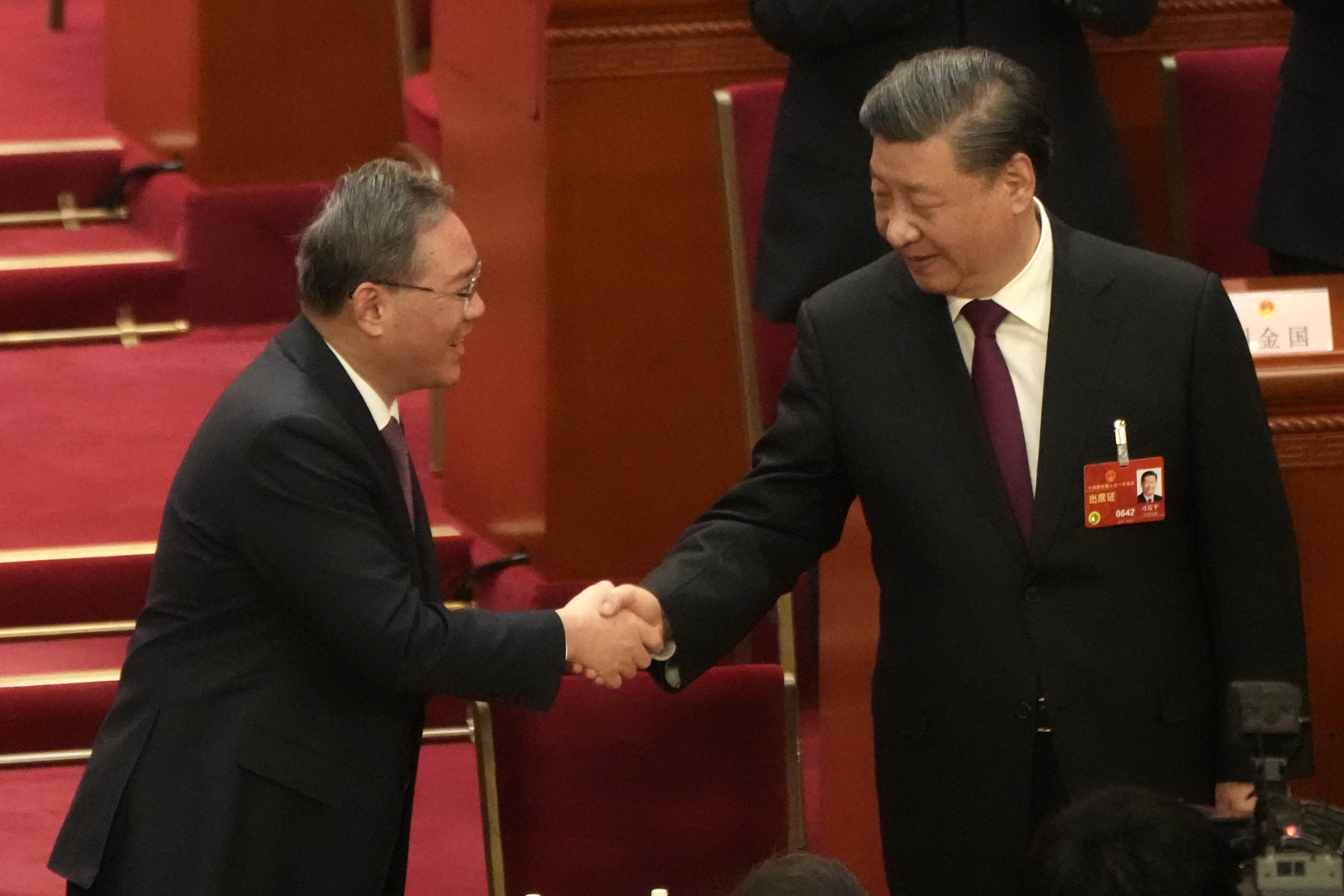 Xi Jinping and Li Qiang shake hands and smile. 