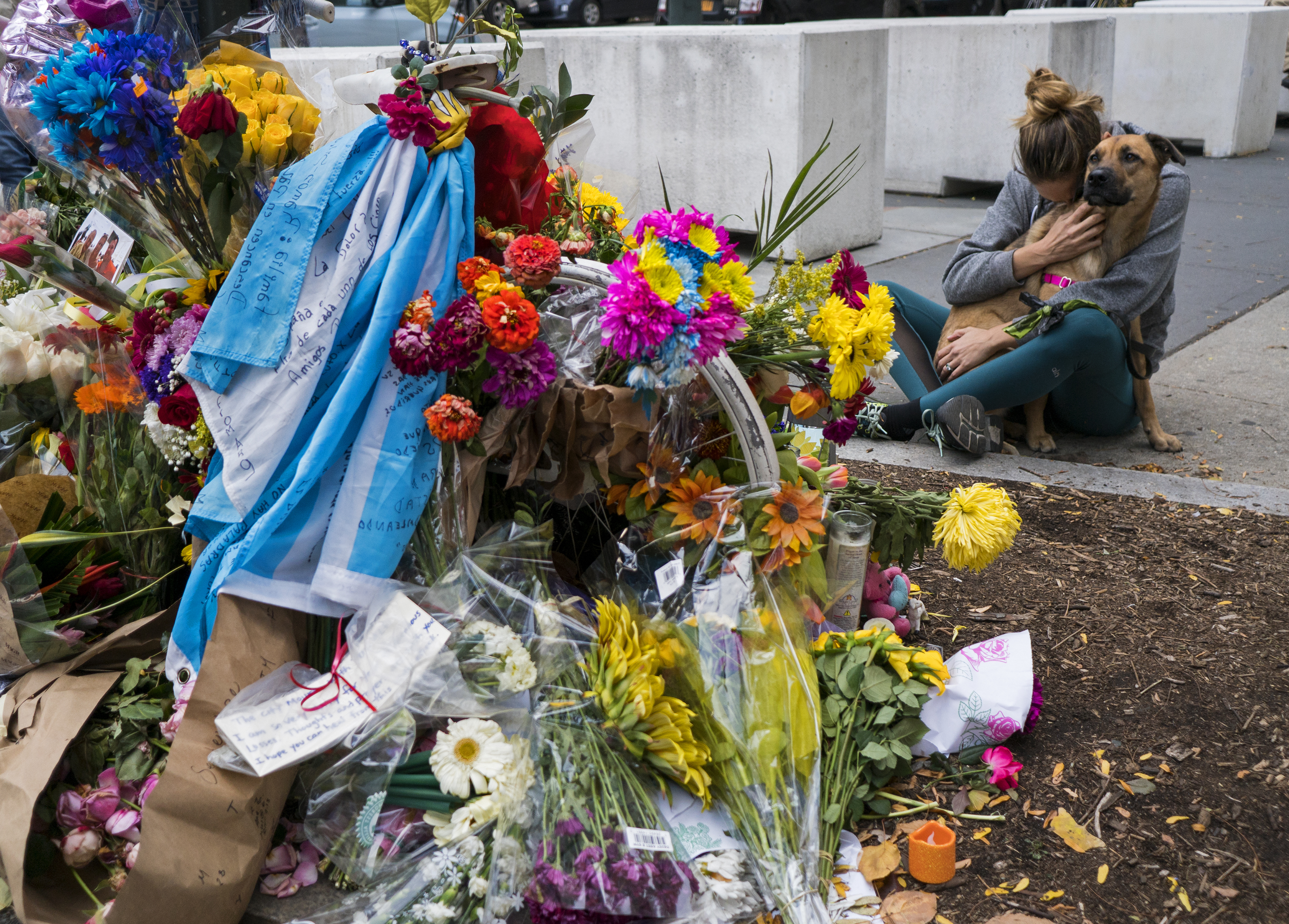 A makeshift tribute of flowers honours the dead in a 2017 attack. A woman is sitting close to the site, hugging her dog in her lap and burying her face in its fur.