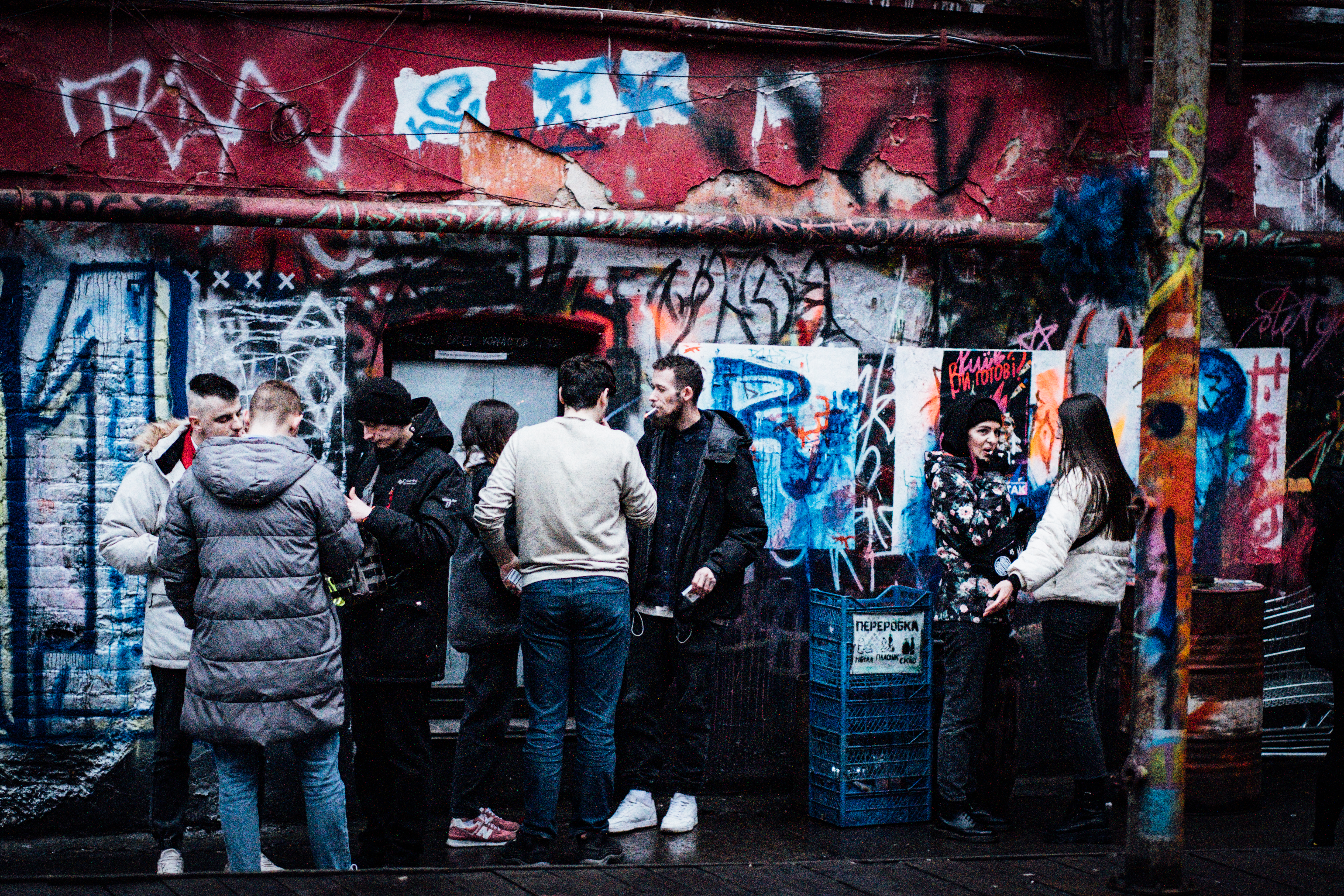 A photo of people standing outside, in front of a wall filled with graffiti.