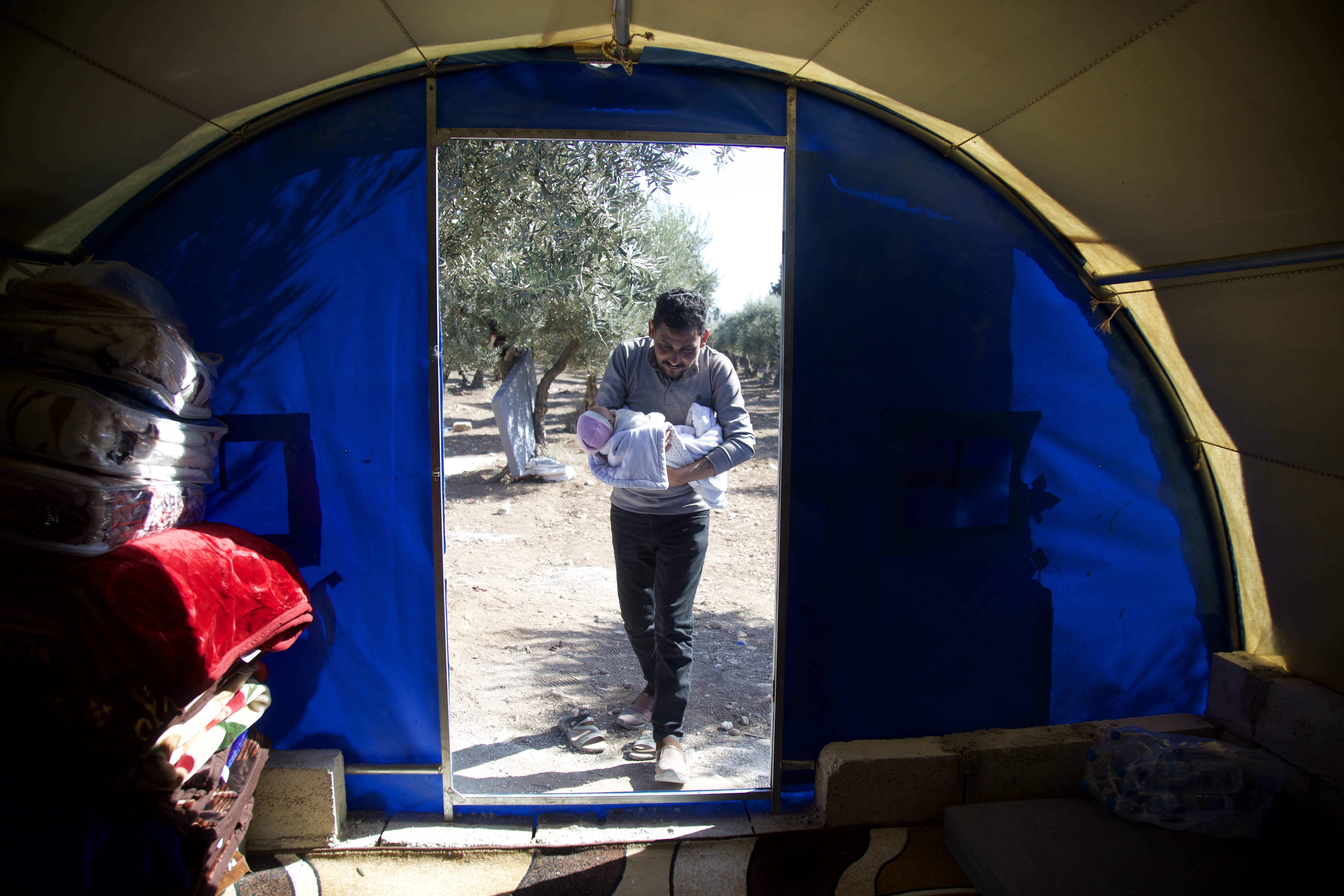 Khalil walks into the family's tent with baby Afraa in his arms