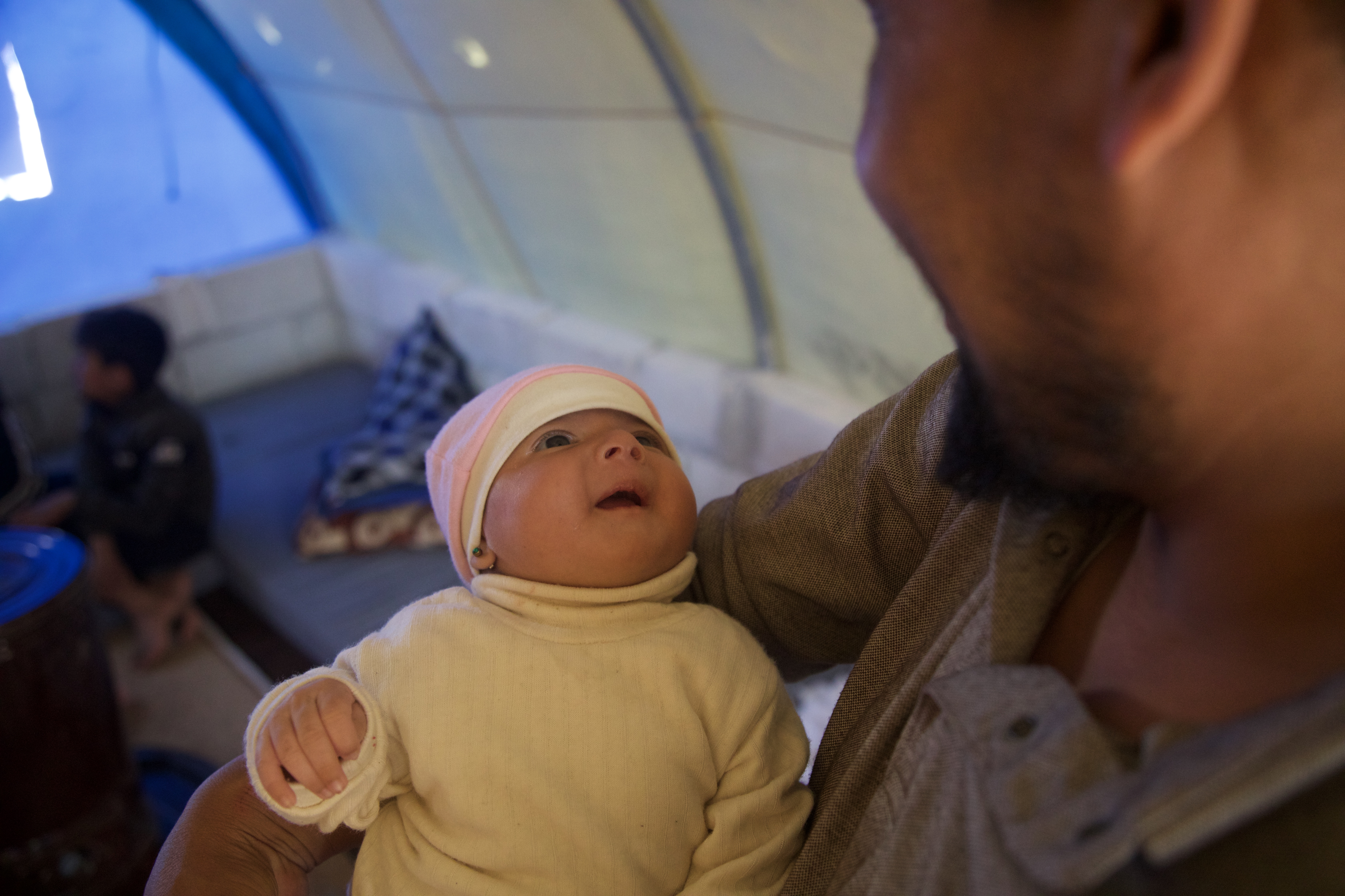 Afraa looks up at her cooing uncle in the family's tent [Ali Haj Suleiman/Al Jazeera]