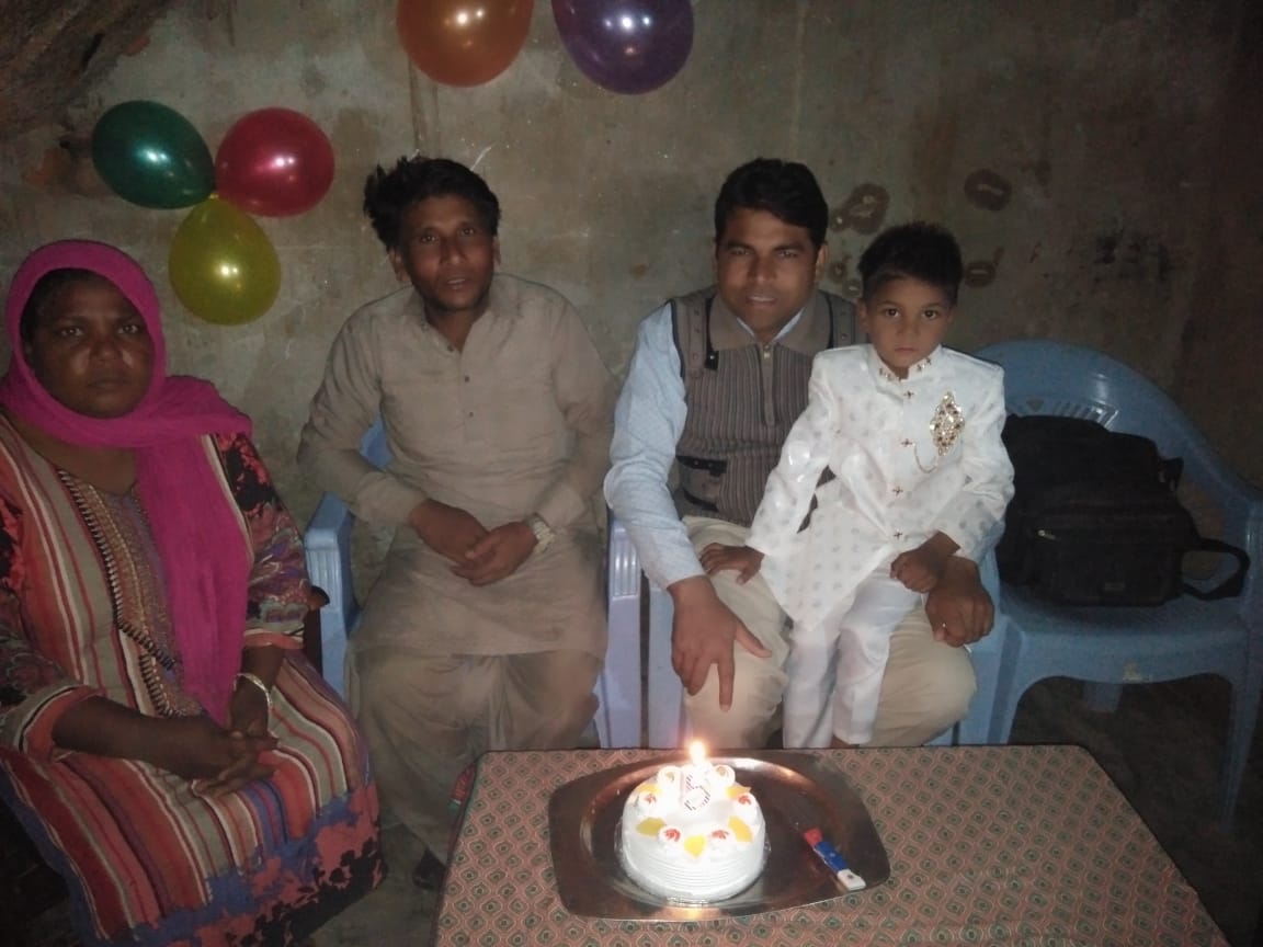 A photo of A photo of a woman with two men sitting on chairs around a birthday cake with a child sitting on the lap of the man on the right wearing a formal outfit.