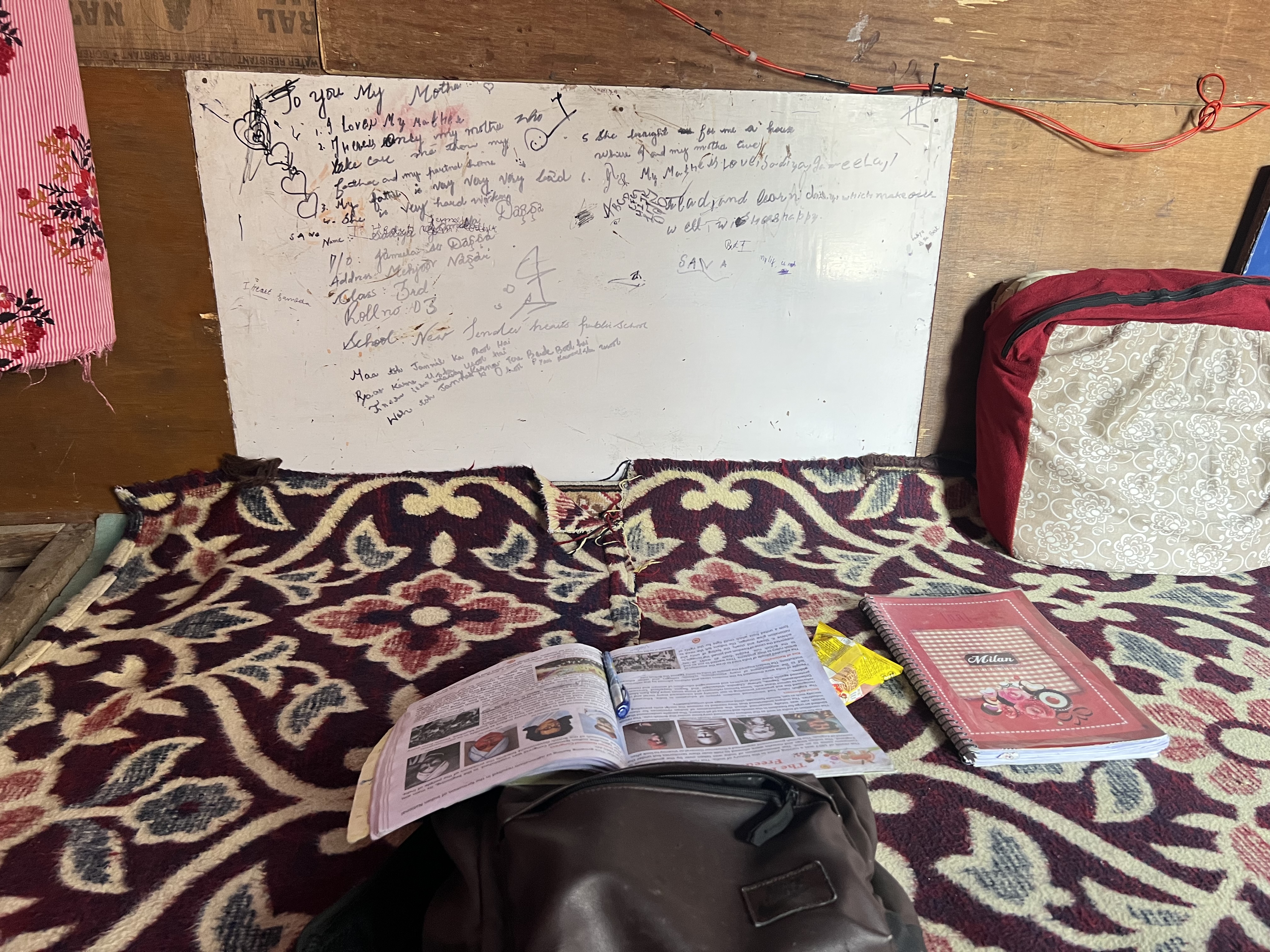 A photo of a white board with writing on it and a textbook laid out in front, on top of a bag.
