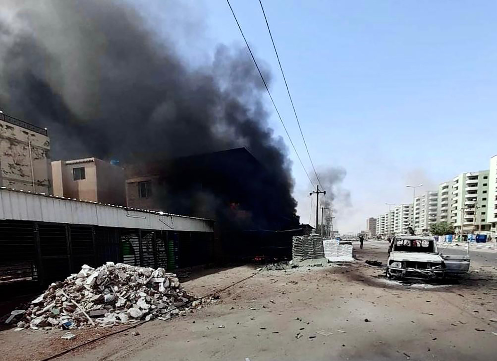 A battle-damaged street in Khartoum, Sudan, with black smoke billowing out of a building.