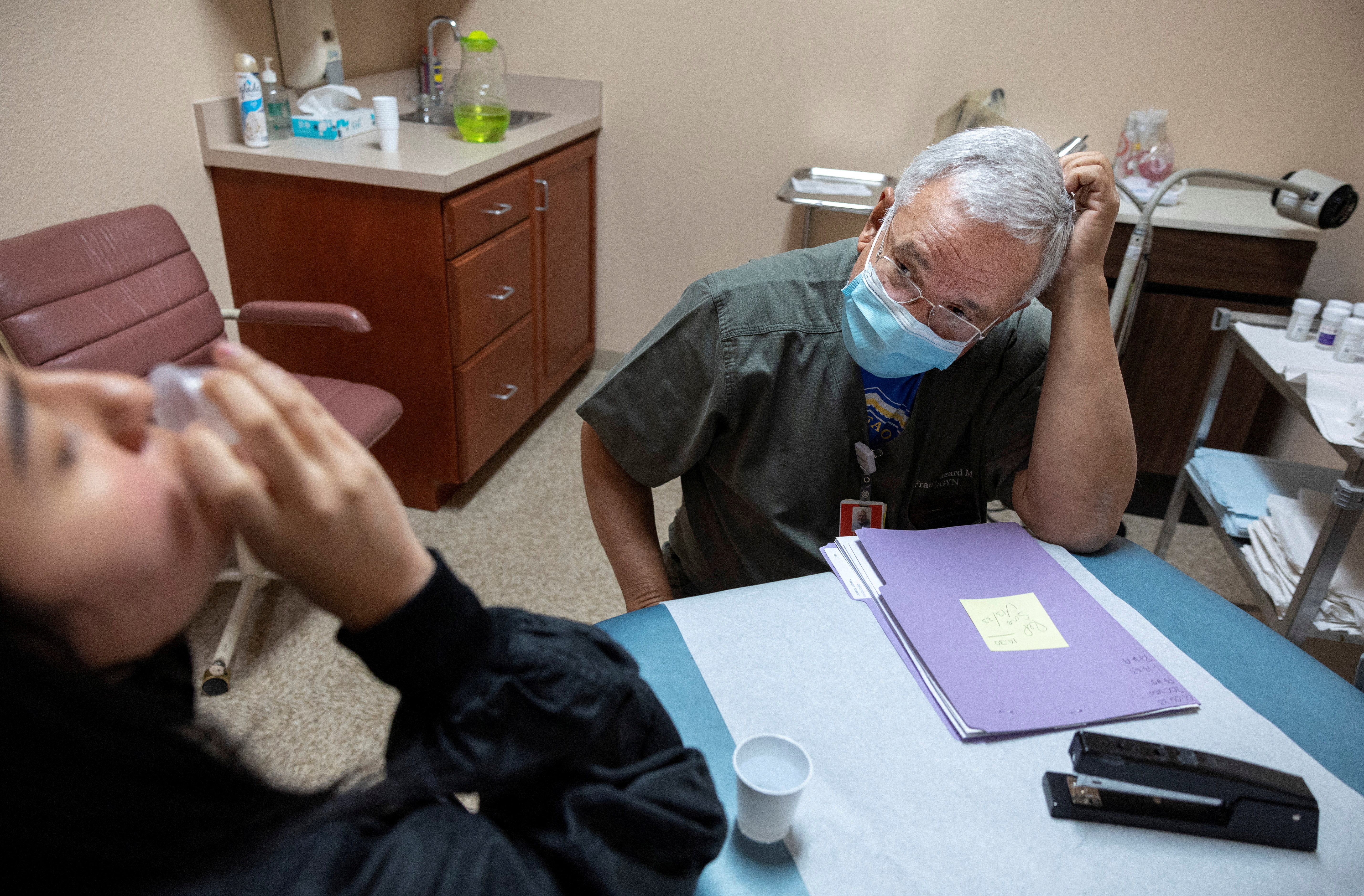 A woman swallows a pill as a doctor watches
