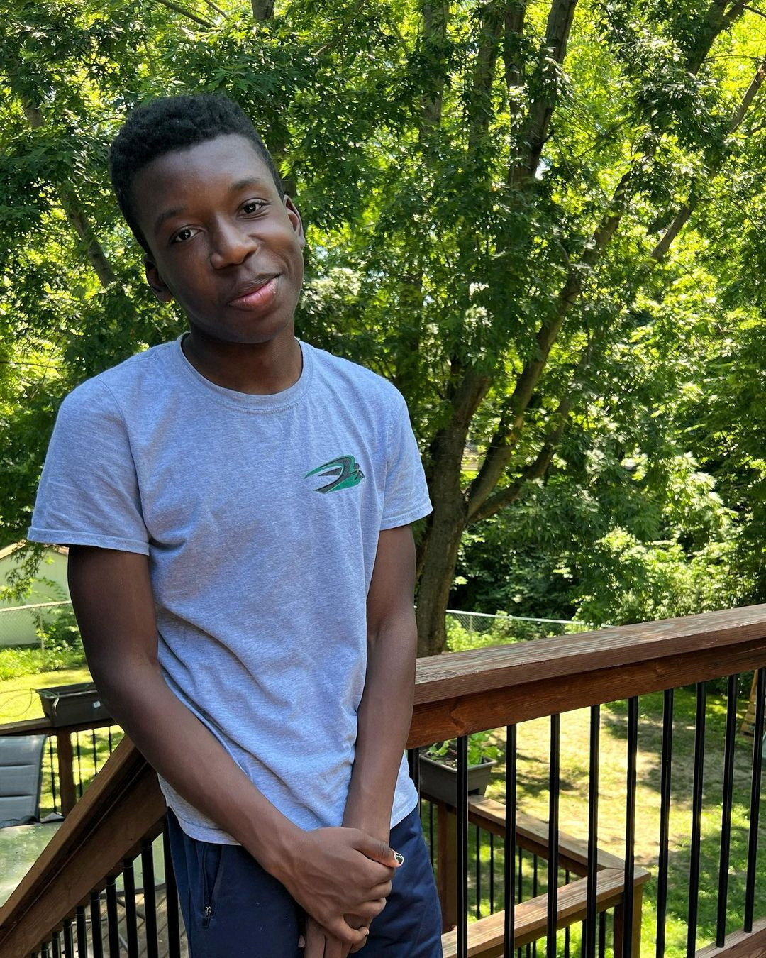 A boy poses outside in a green space against a railing