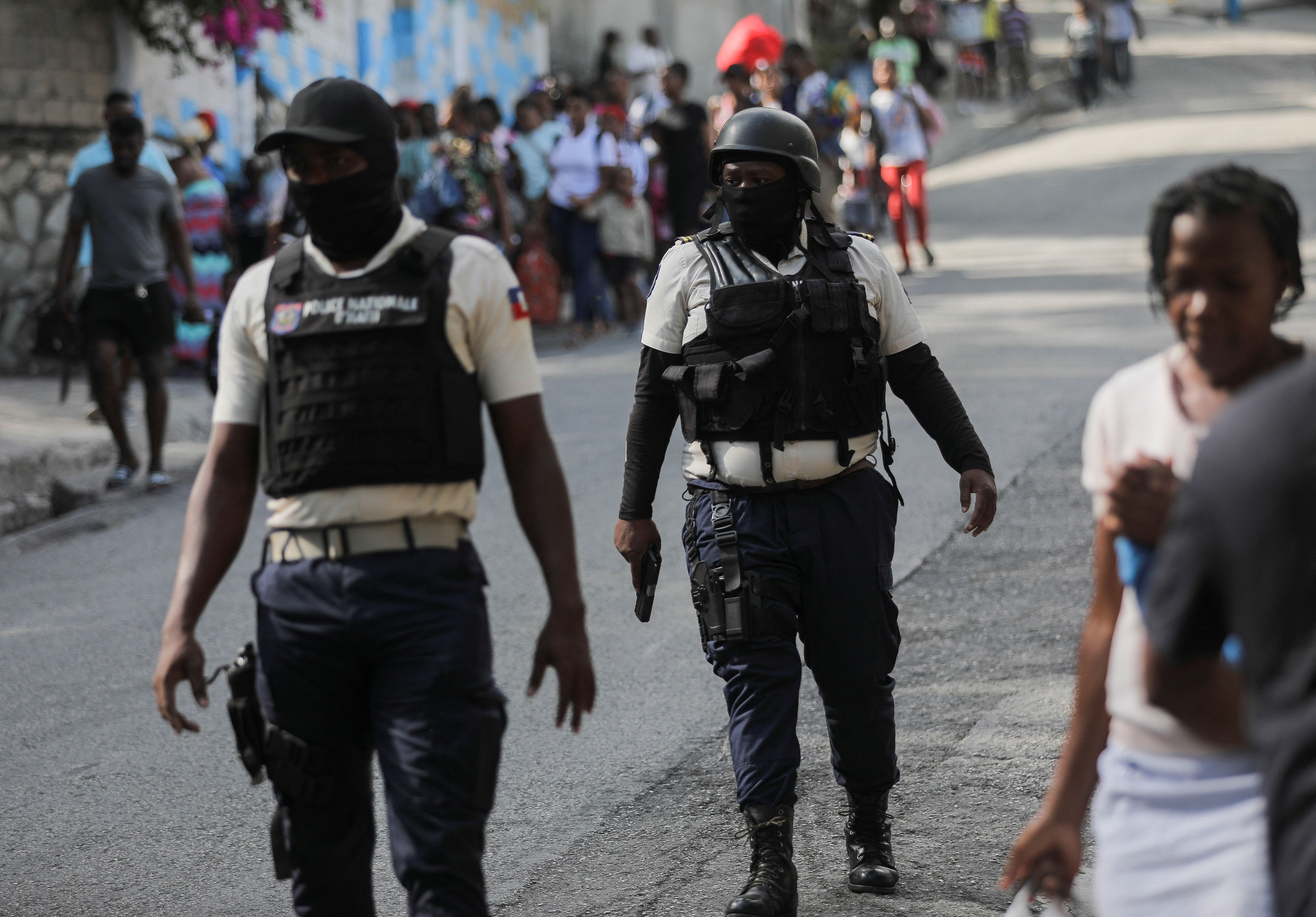 Police officers walk near people carrying their belongings amid gang violence in Haiti's capital Port-au-Prince