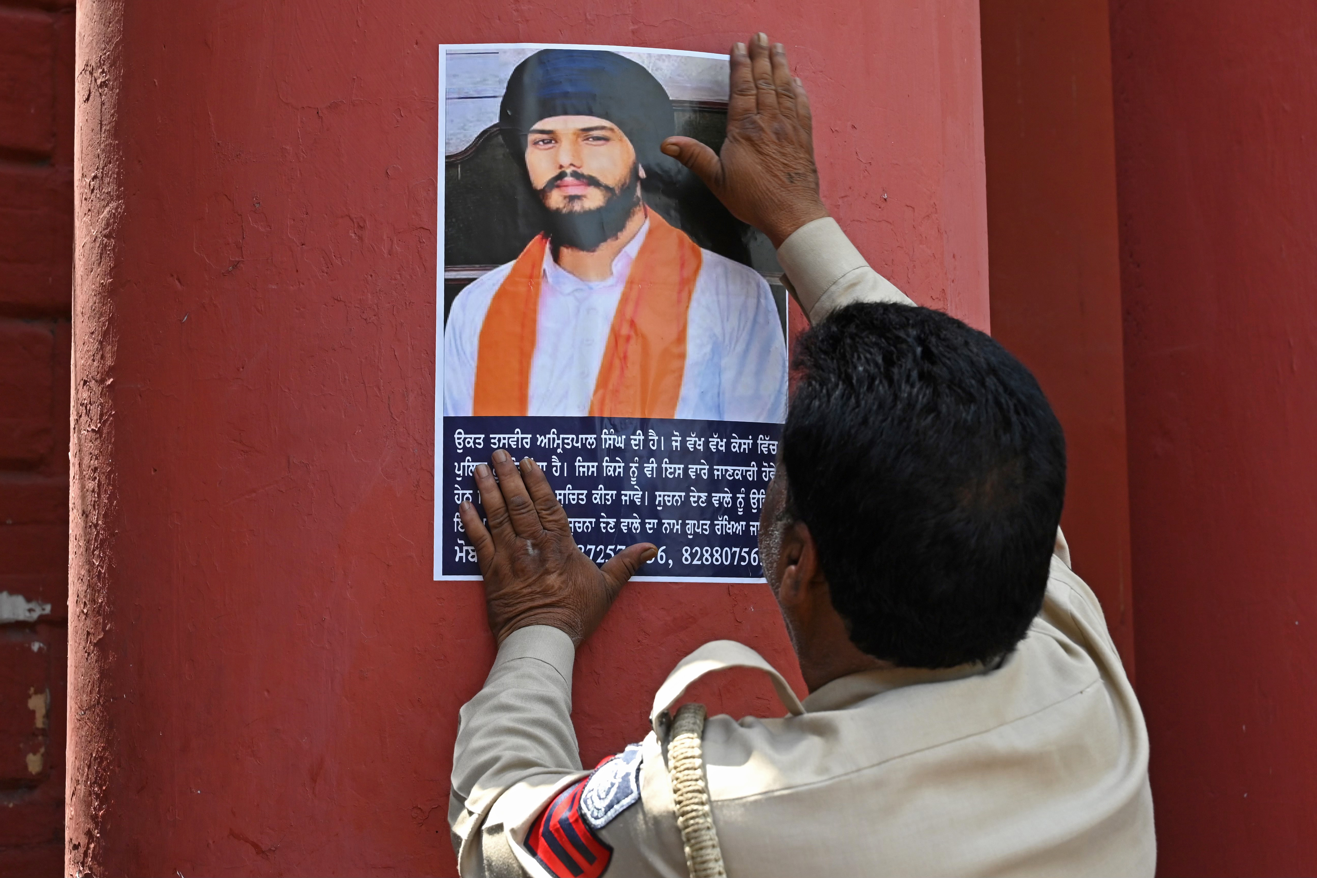 Police stick Amritpal Singh's poster at a railway station in Amritsar on April 13, 2023. - A firebrand fugitive Sikh separatist has posted a video taunting Indian authorities after a fruitless almost two-week manhunt involving thousands of police and internet shutdowns.