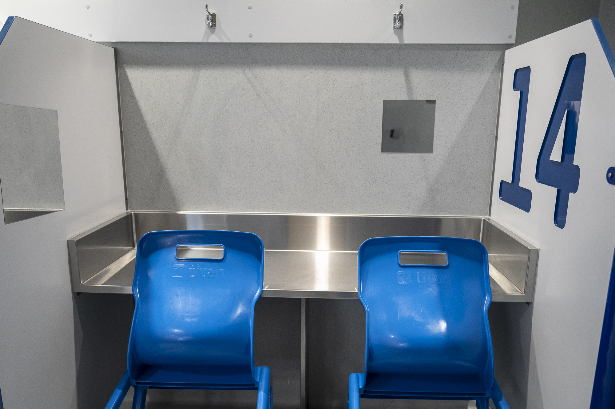 The cubicle has a steel table and two blue chairs. There is a large number 14 on the right-hand side of the partition wall.