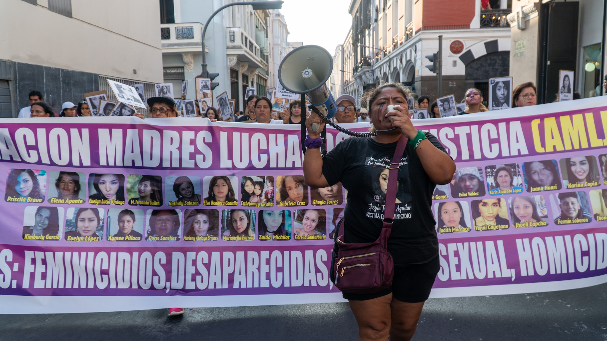 Magali Aguilar speaks into a bullhorn as women carry a banner featuring the faces of women who have faced gender-based violence