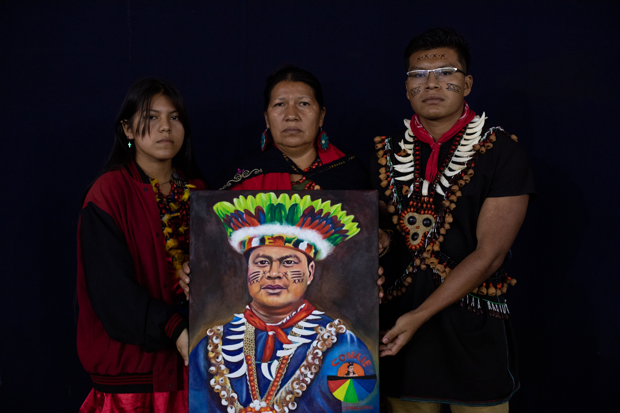A woman with two children on either side of her holds a painted portrait of Eduardo Mendúa