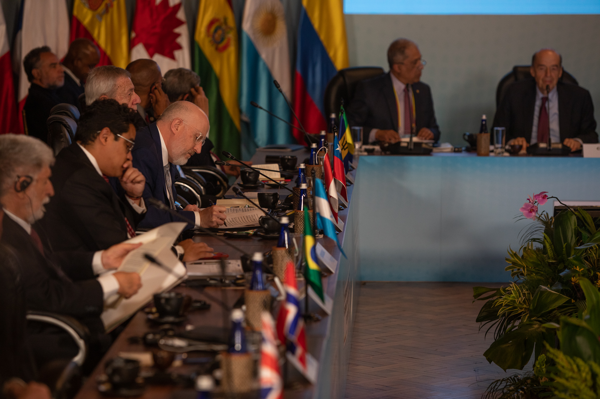 Participants in the conference sit next to each other with flags in the background