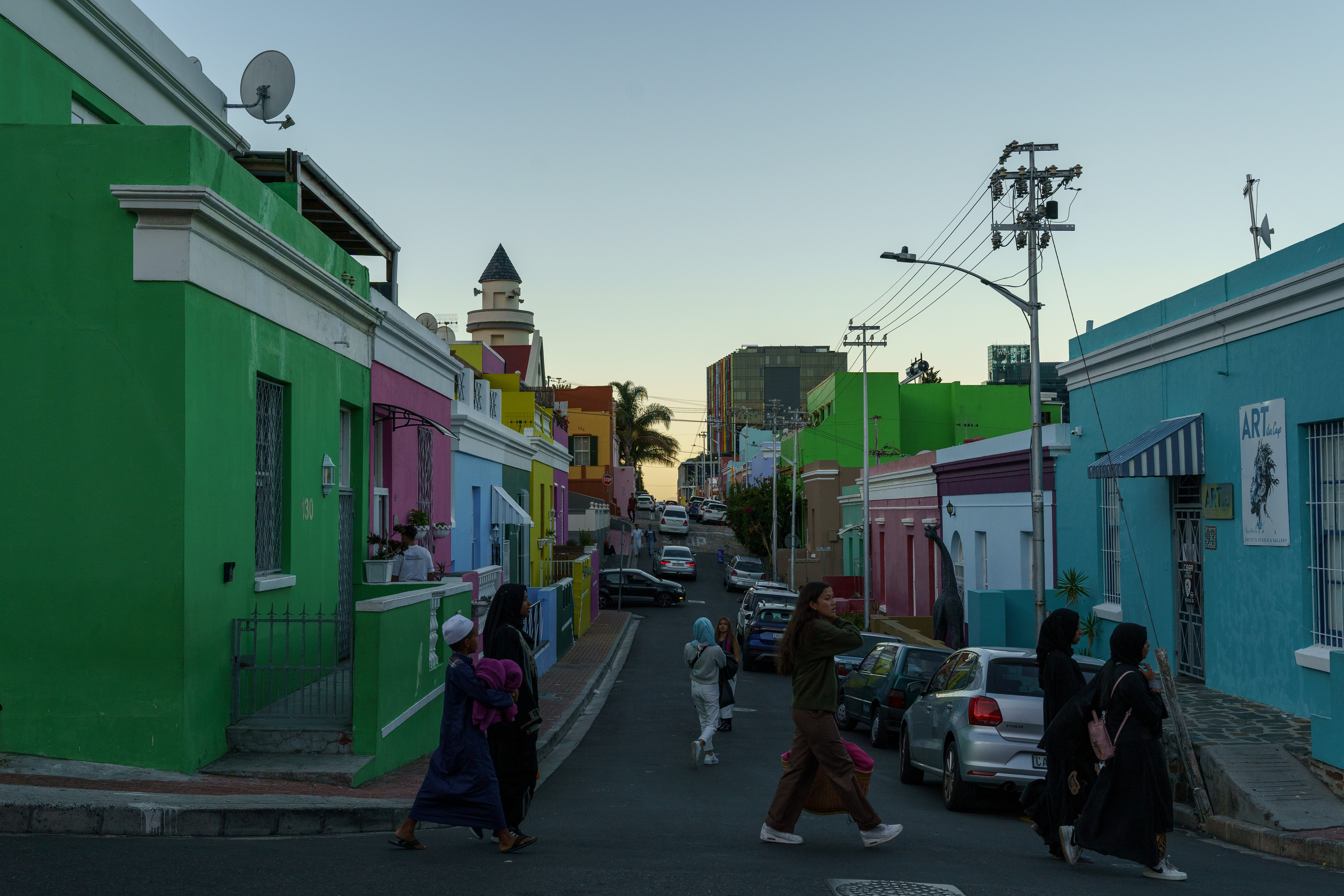 A photo of a neighborhood with colourful buildings and people walking across the street.