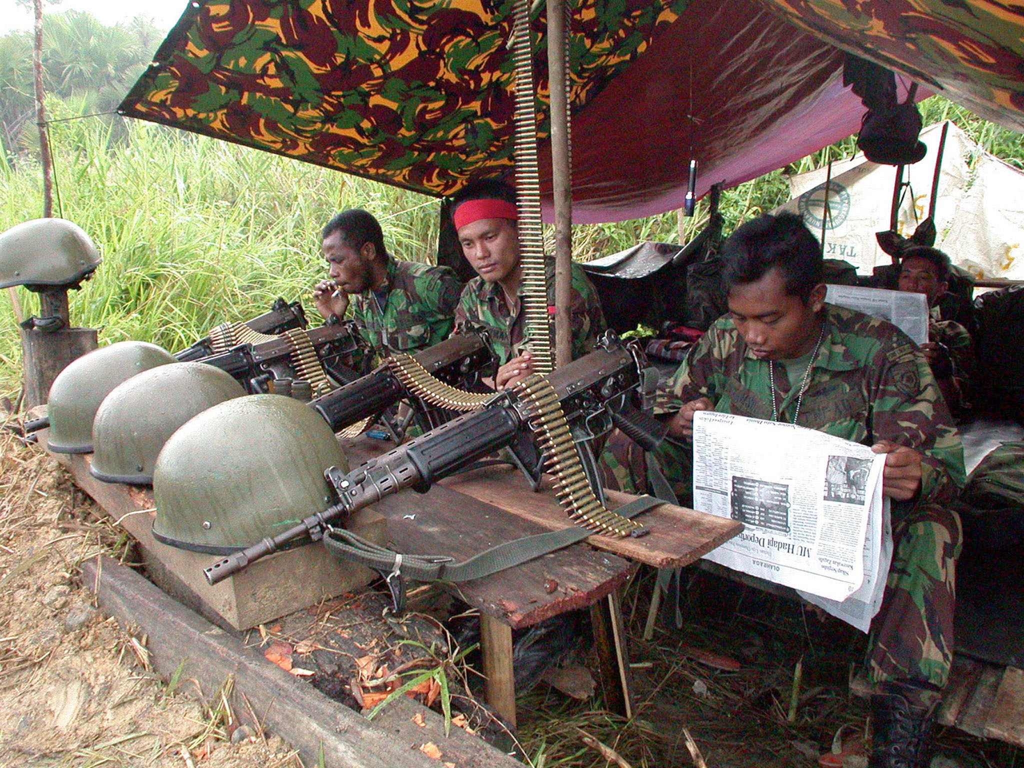 Indonesian soldiers in a shelter during the Aceh conflict in 2002. They have taken their helmets off and laid their weapons on the table in front of them