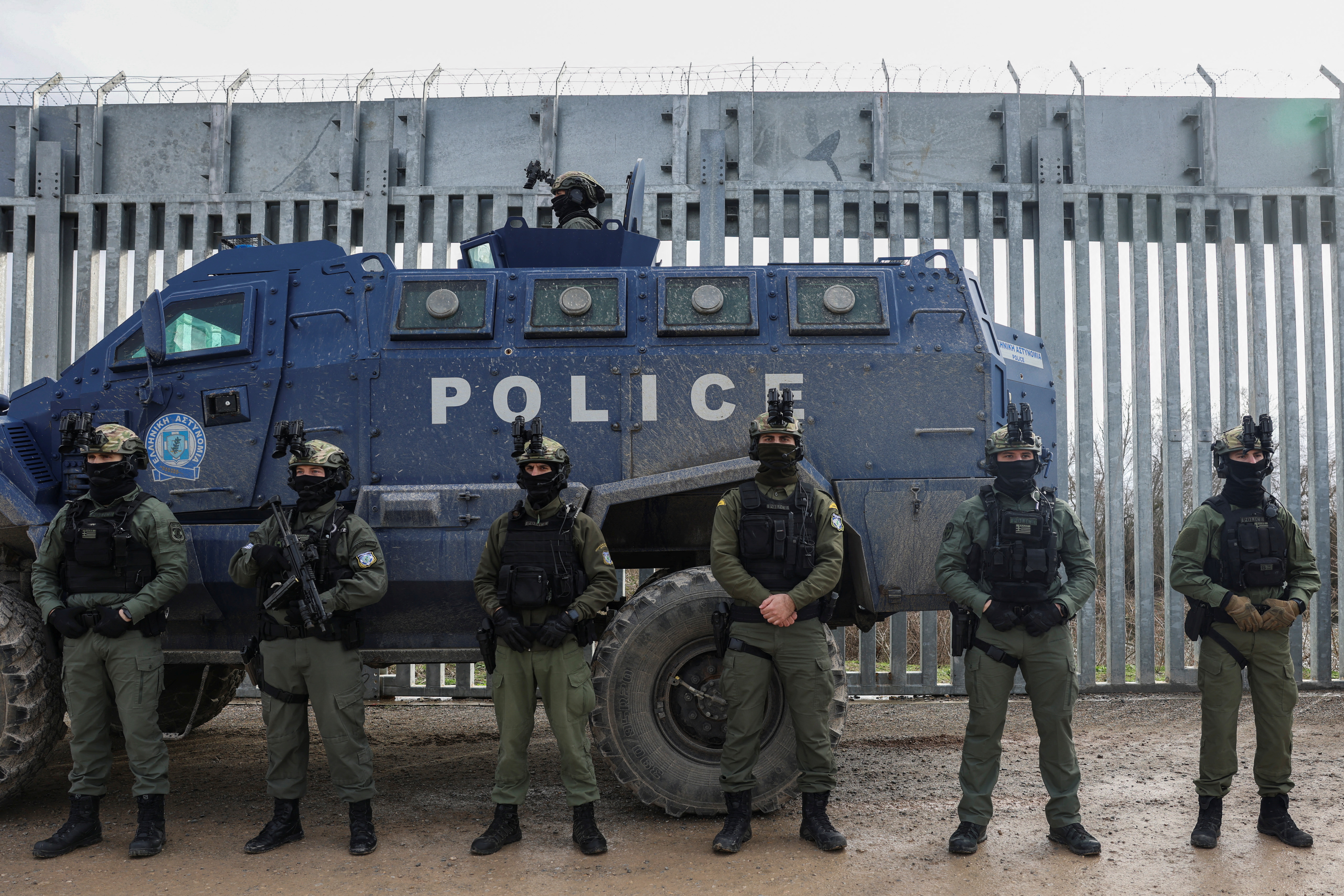 Greek police officers line up next to a border fence