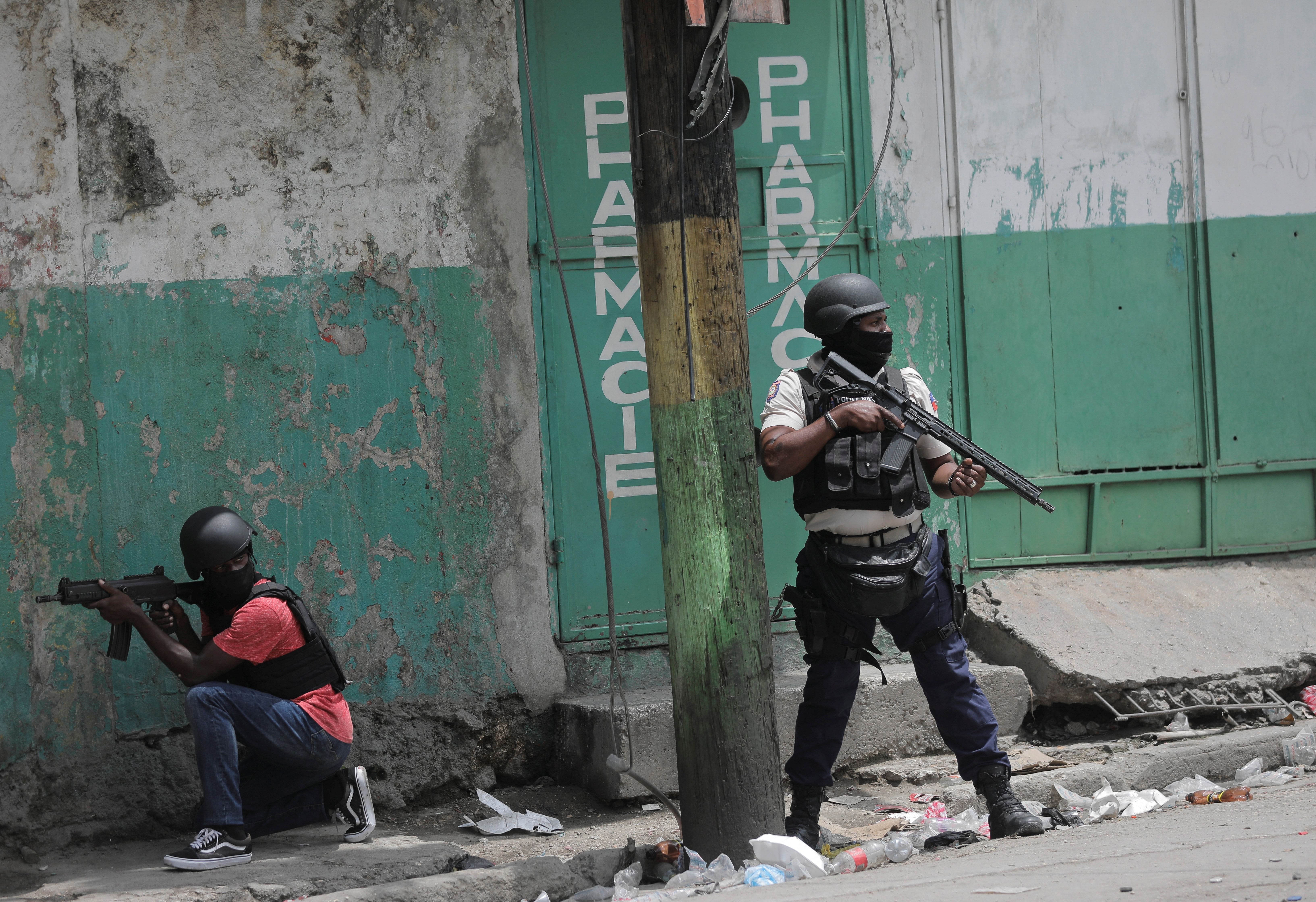 Police officers with helmets, protective vests and riffles stand in desolate street near a white and green wall