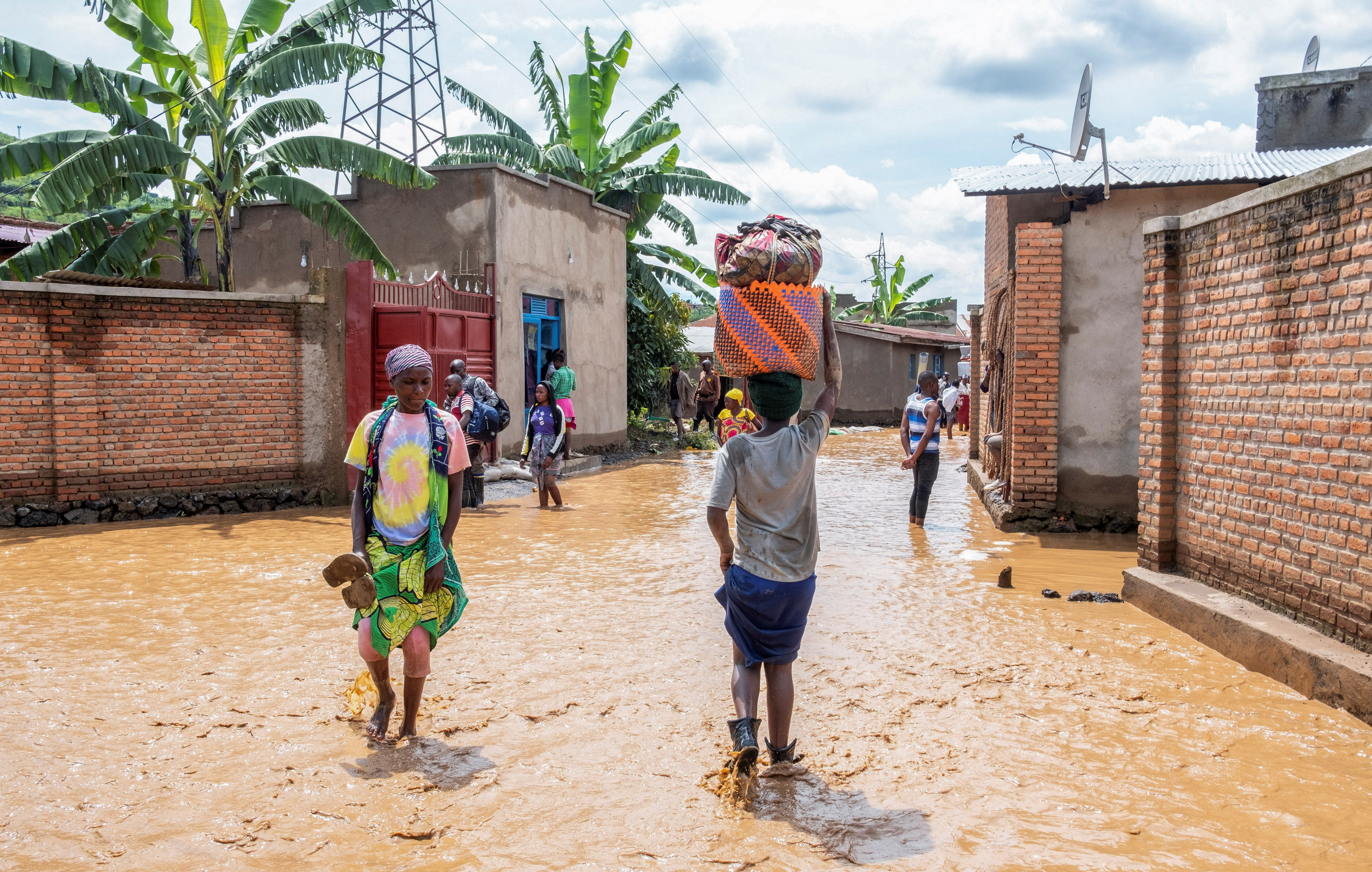 Residents wade through water after their homes were swamped following rains that triggered flooding and landslides in Rubavu district
