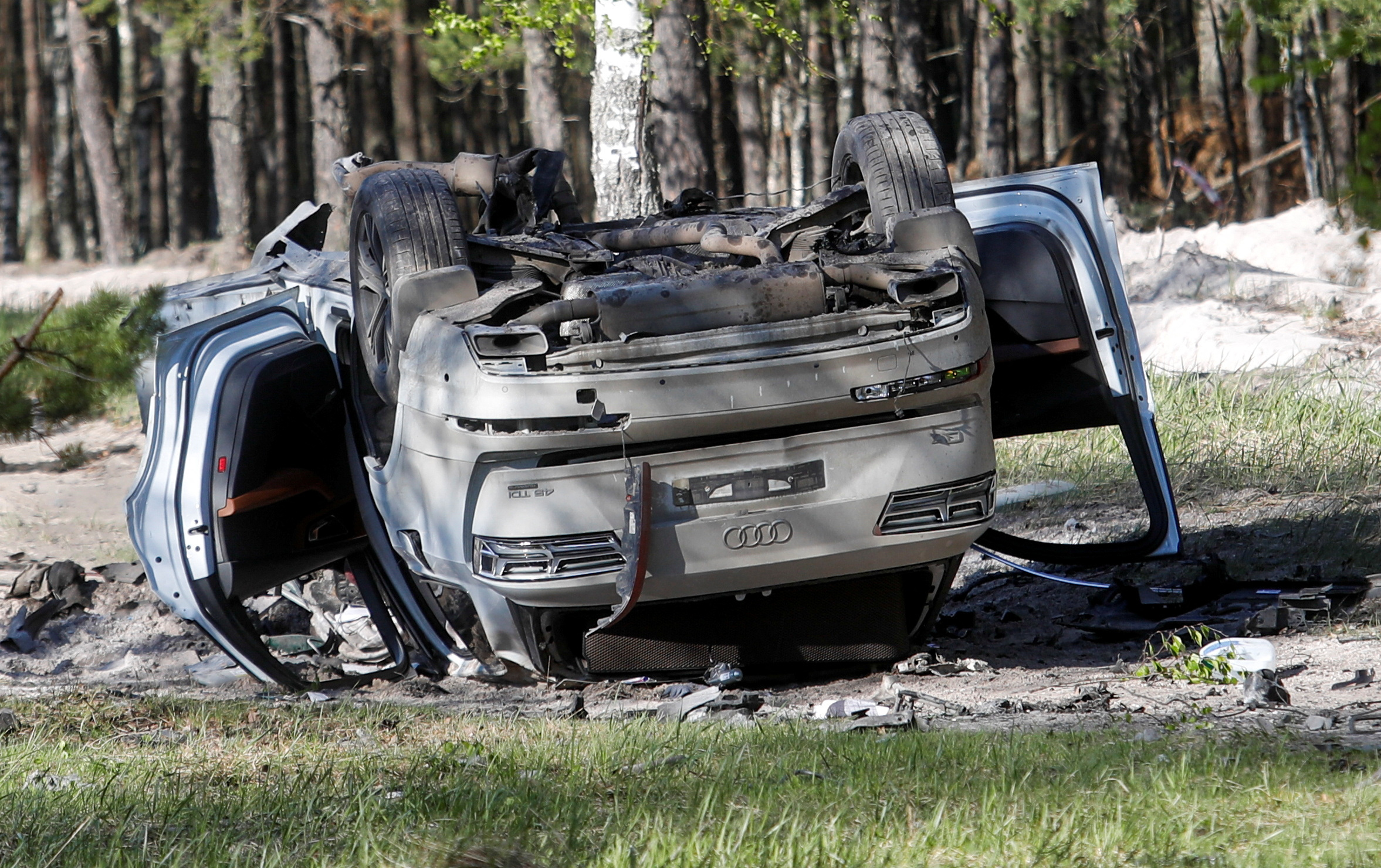 Zakhar Prilepin's car lies overturned on a track next to the woods after a bomb blast.