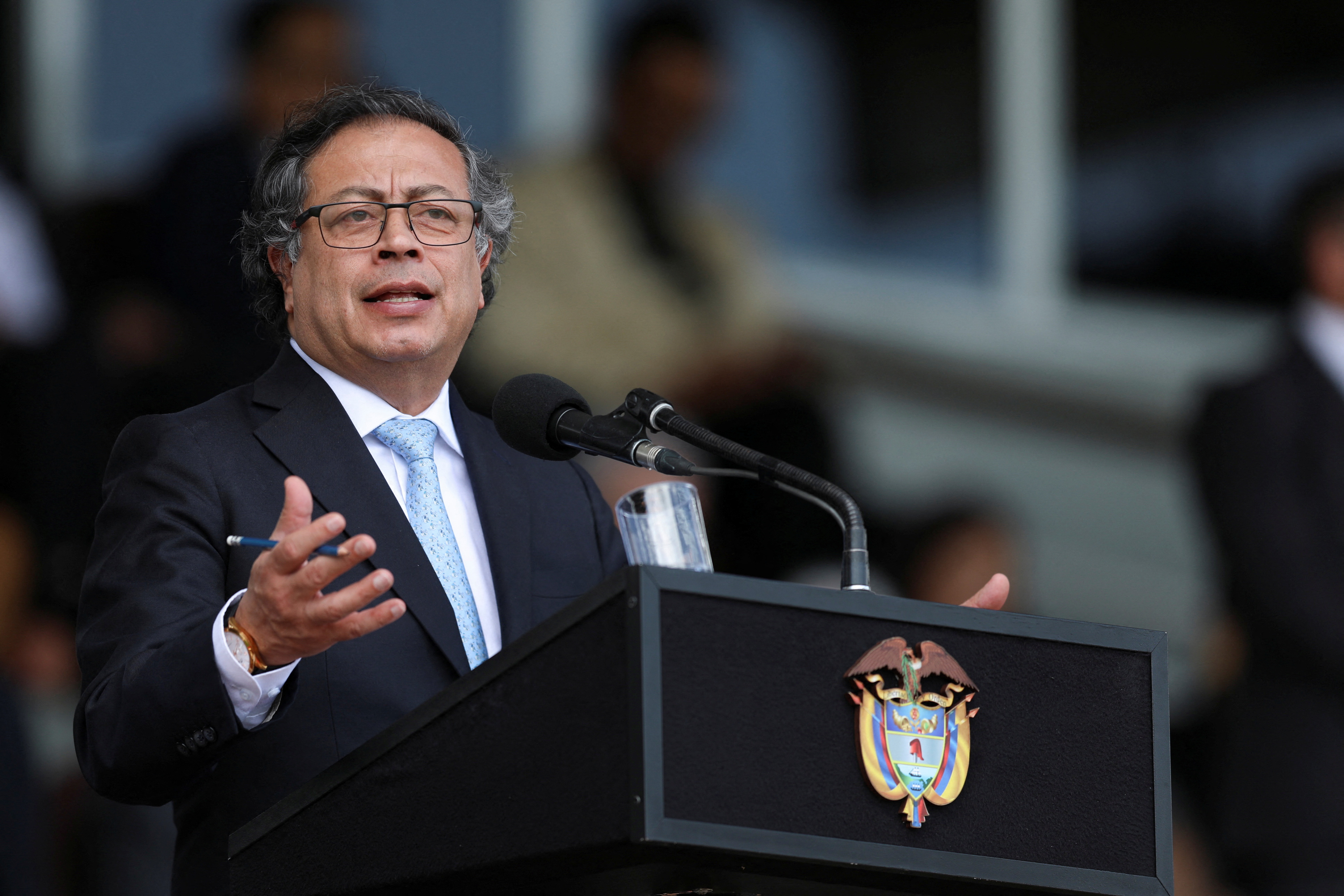 A man dressed in a suit and tie gestures broadly from behind an official government podium in Bogota, Colombia