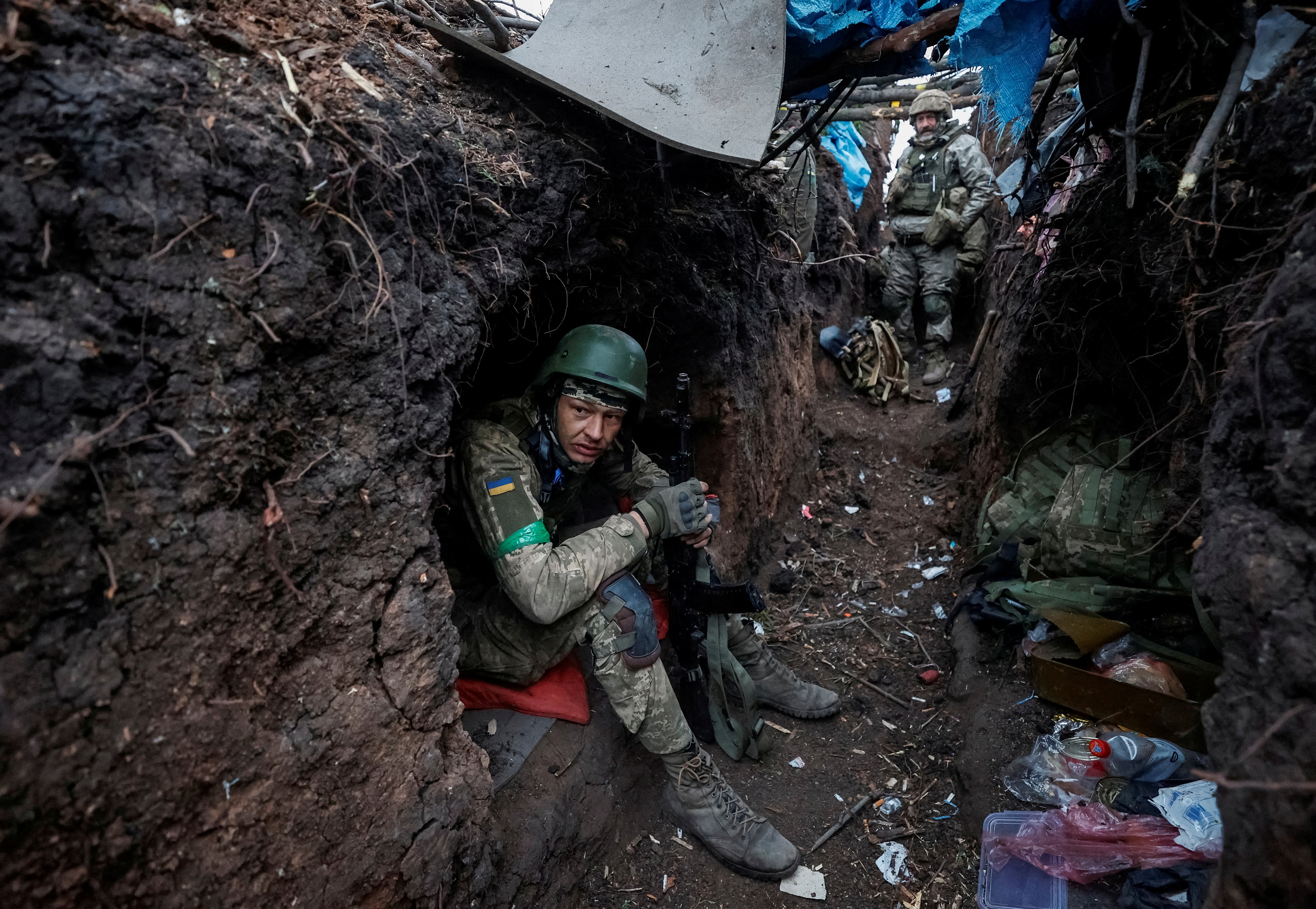 A Ukrainian soldier takes a rest in a trench near the front line in Bakhmut, Ukraine. Other soldiers are behind him in the trench.