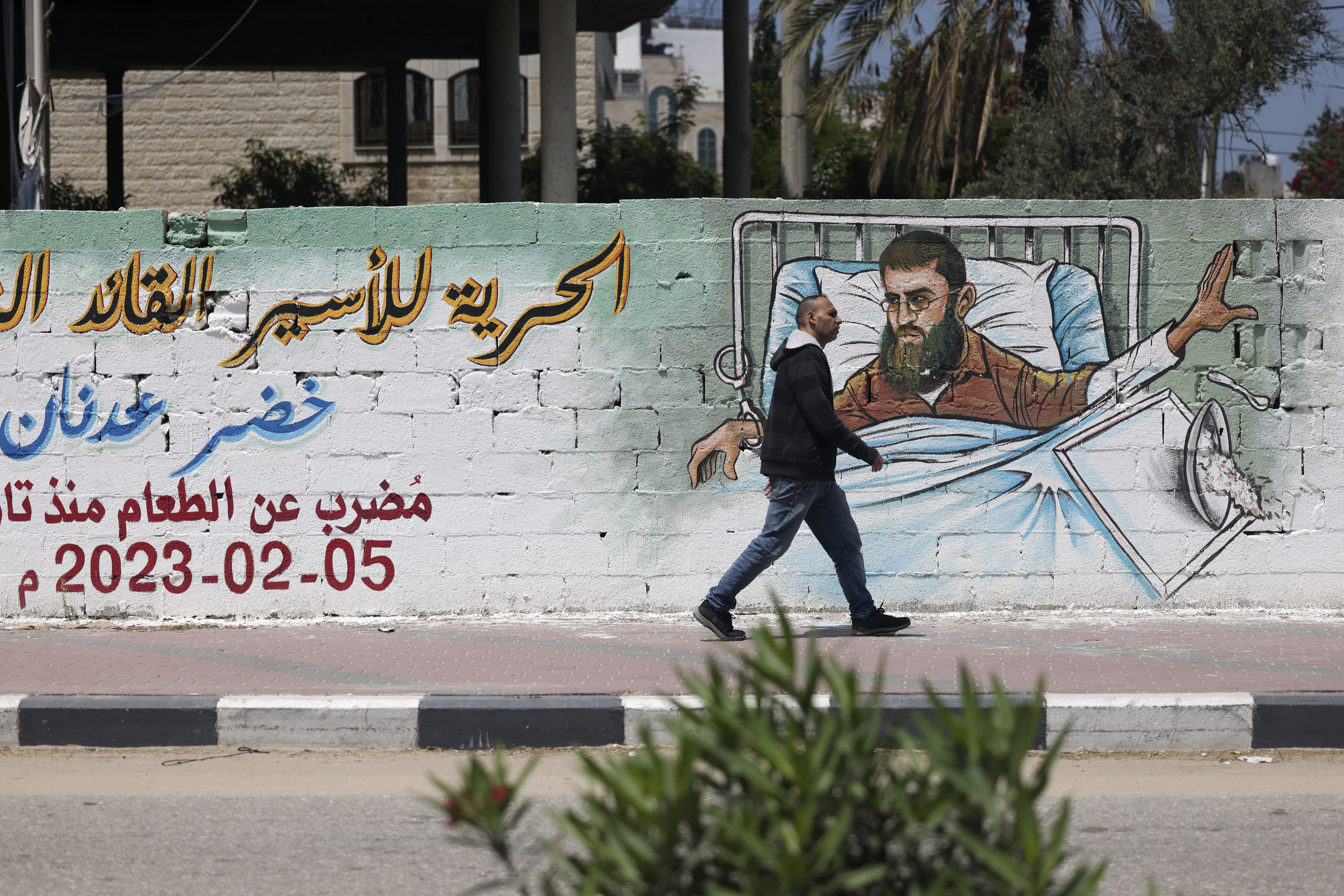A Palestinian man walks past a graffiti of Khader Adnan, a hunger-striking Palestinian imprisoned in an Israeli jail, in Gaza City on April 17, 2023. (Photo by Mohammed ABED / AFP)